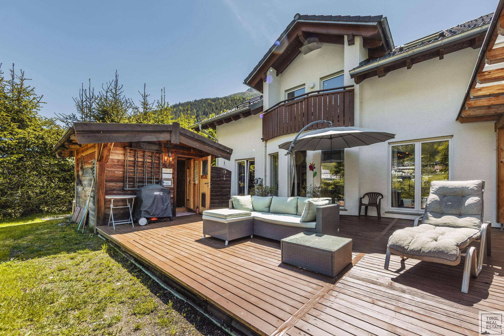 Sonnige Holzterrasse mit Gartenmöbeln und einem Gartenhaus, ideal zum Entspannen.