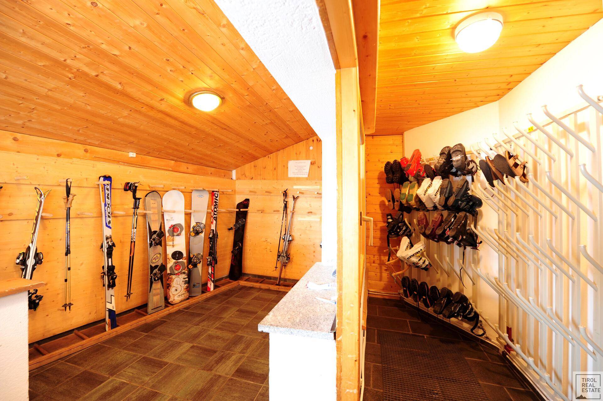 Skiraum mit Holzverkleidung, Fliesenboden und Halterungen für Skier und Skischuhe.