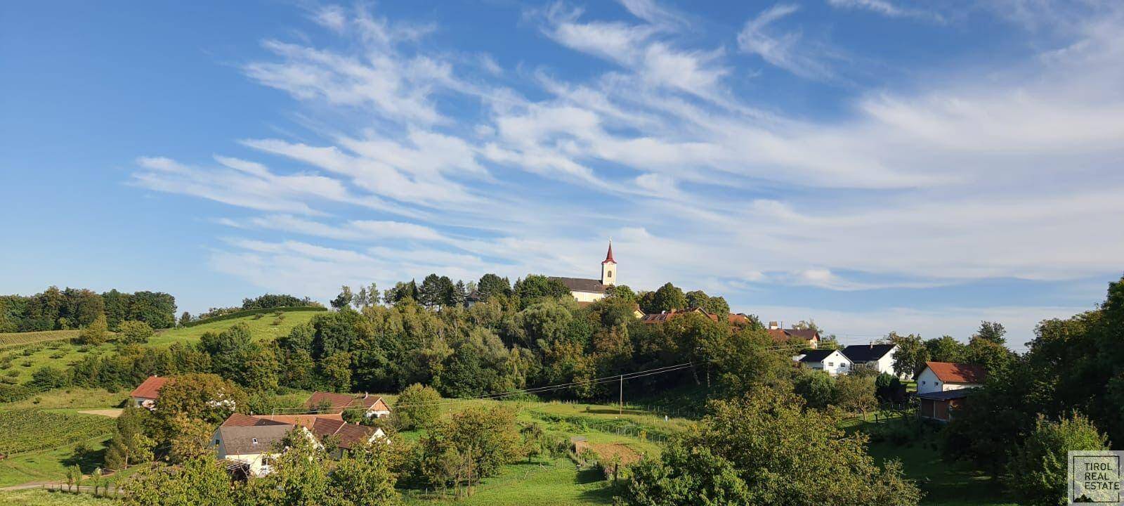 Malerische Landschaft mit einem Dorf und einer Kirche auf einem Hügel unter blauem Himmel.