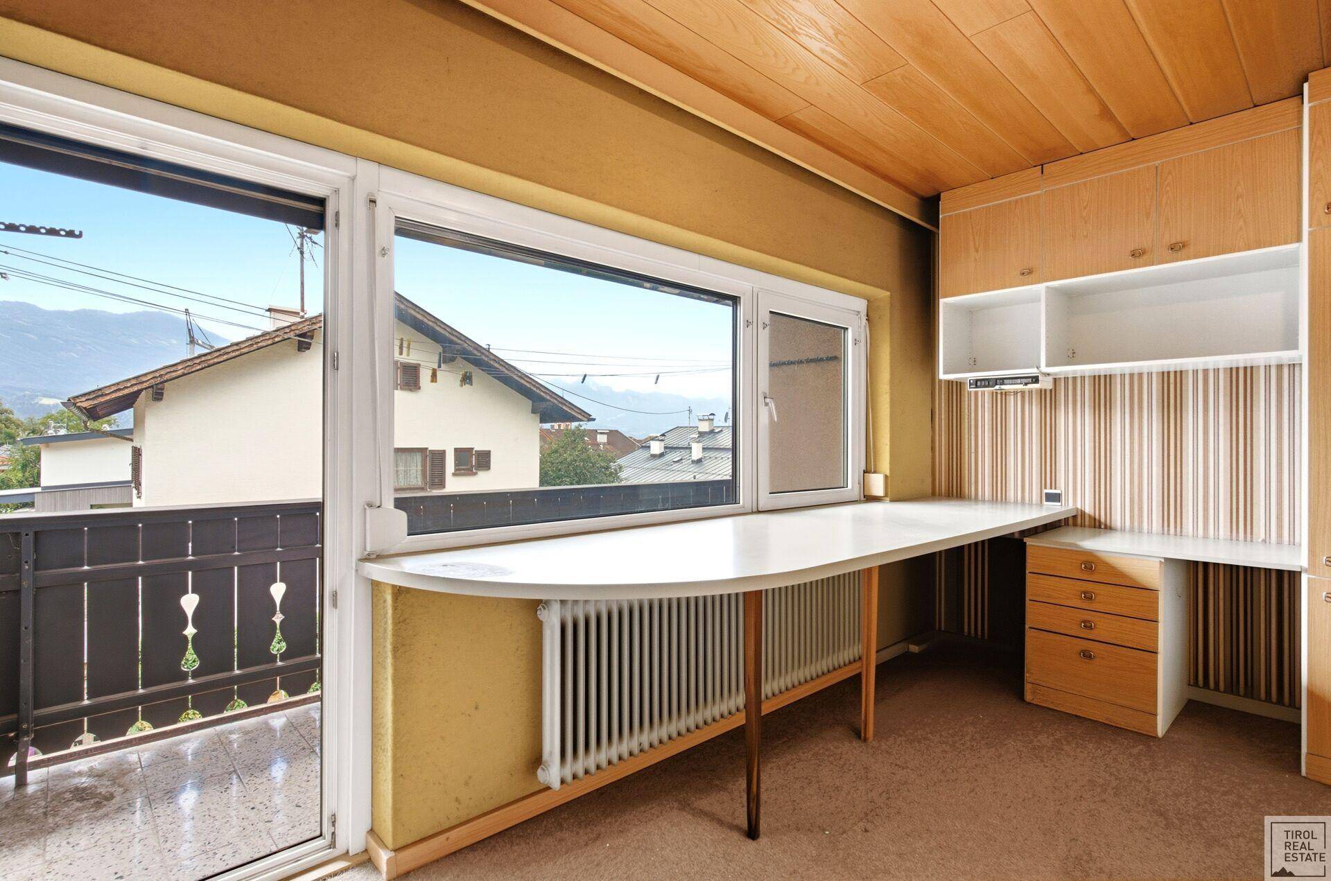 Innenraum mit langer Arbeitsfläche am Fenster und Zugang zu einem Balkon mit Bergblick.