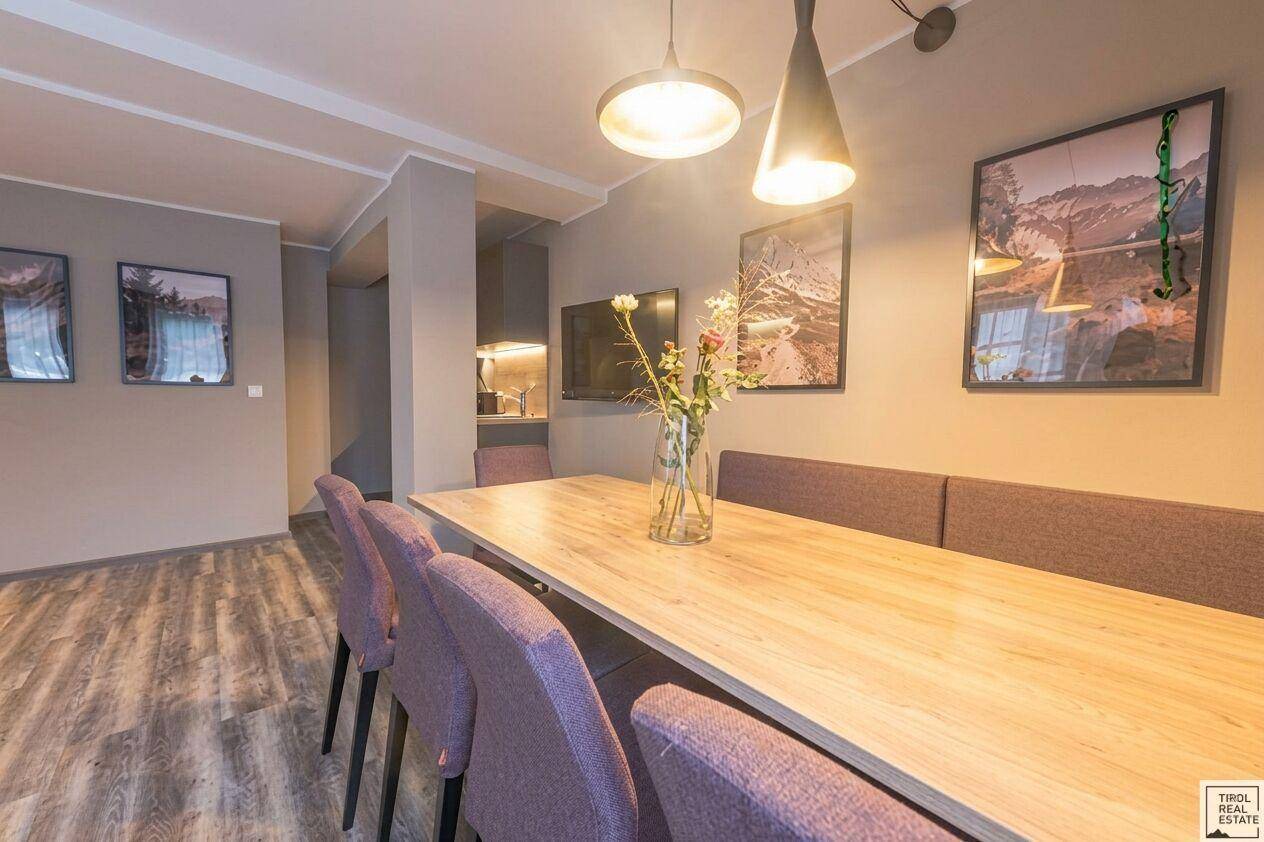 Heller Essbereich mit großem Holztisch und lila Stühlen, angrenzend an eine moderne Küche.