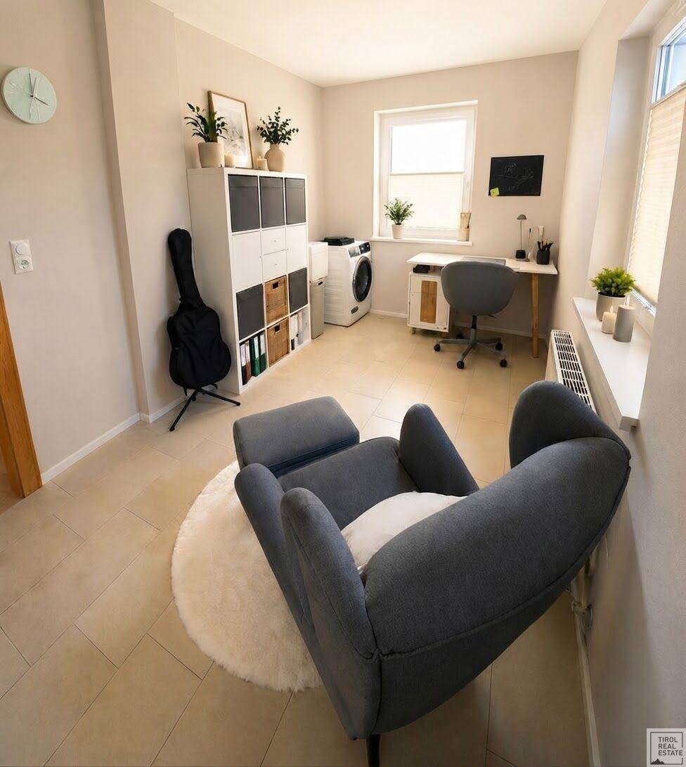 Helles Arbeitszimmer mit Schreibtisch, Sessel und einer Waschmaschine, ideal als Mehrzweckraum nutzbar.