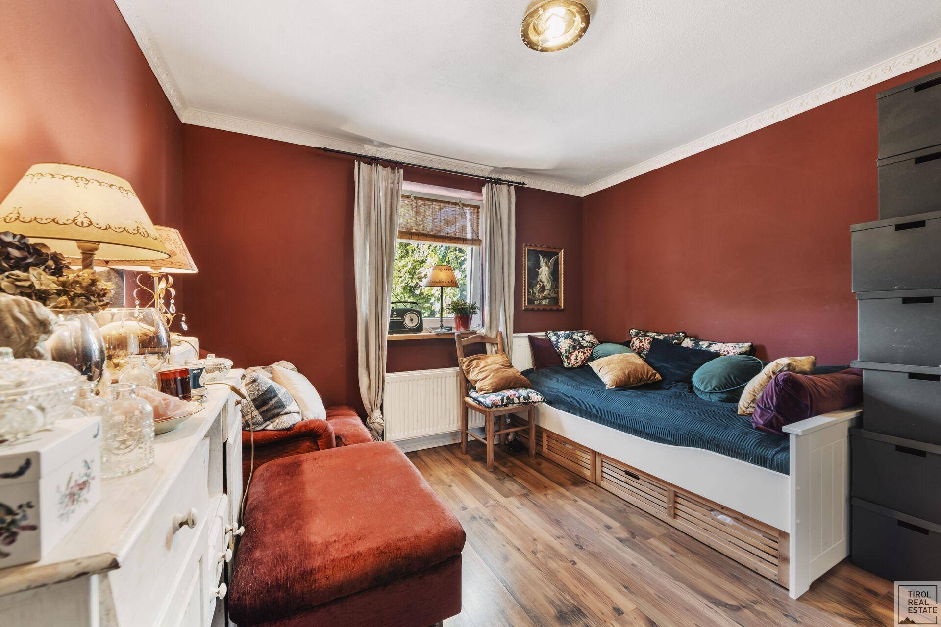 Farbenfrohes Schlafzimmer mit roten Wänden, Holzboden und einem bequemen Tagesbett.