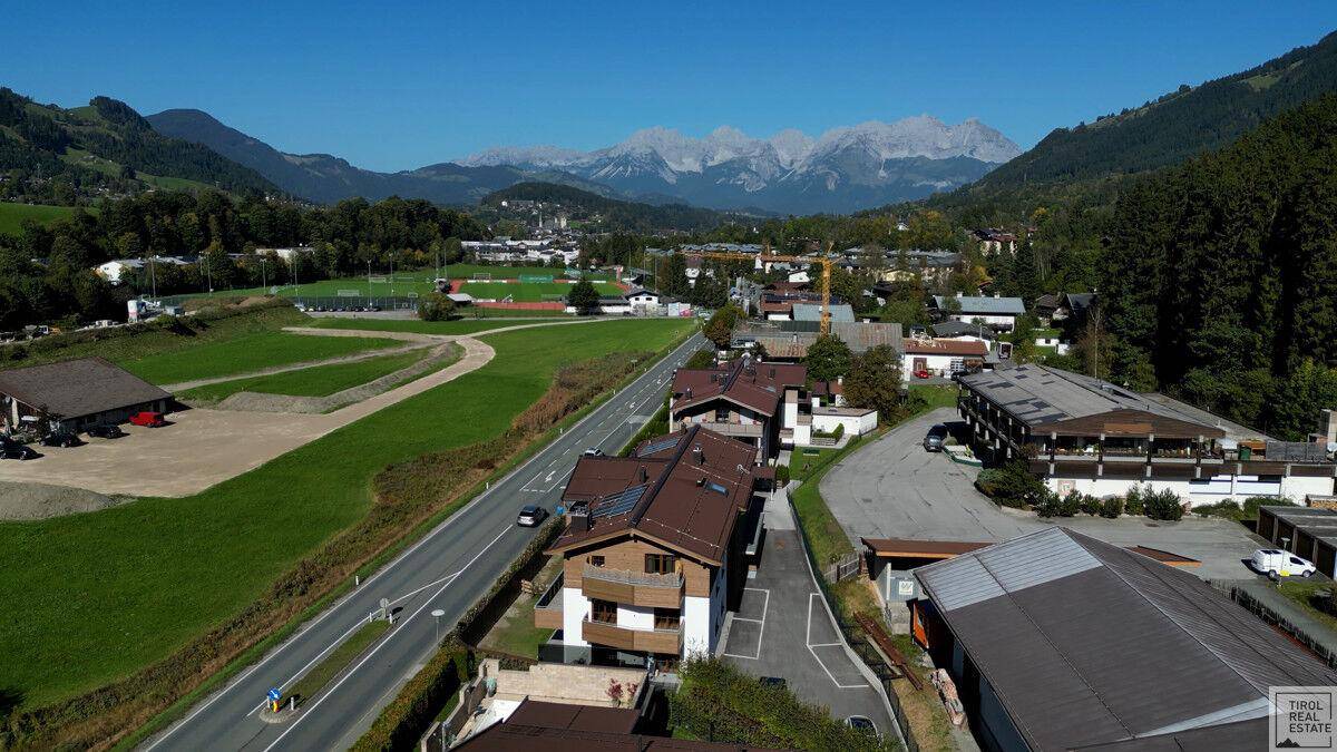 Weitläufige Landschaft mit Wohngebäuden, Sportplätzen und majestätischen Bergen im Hintergrund.