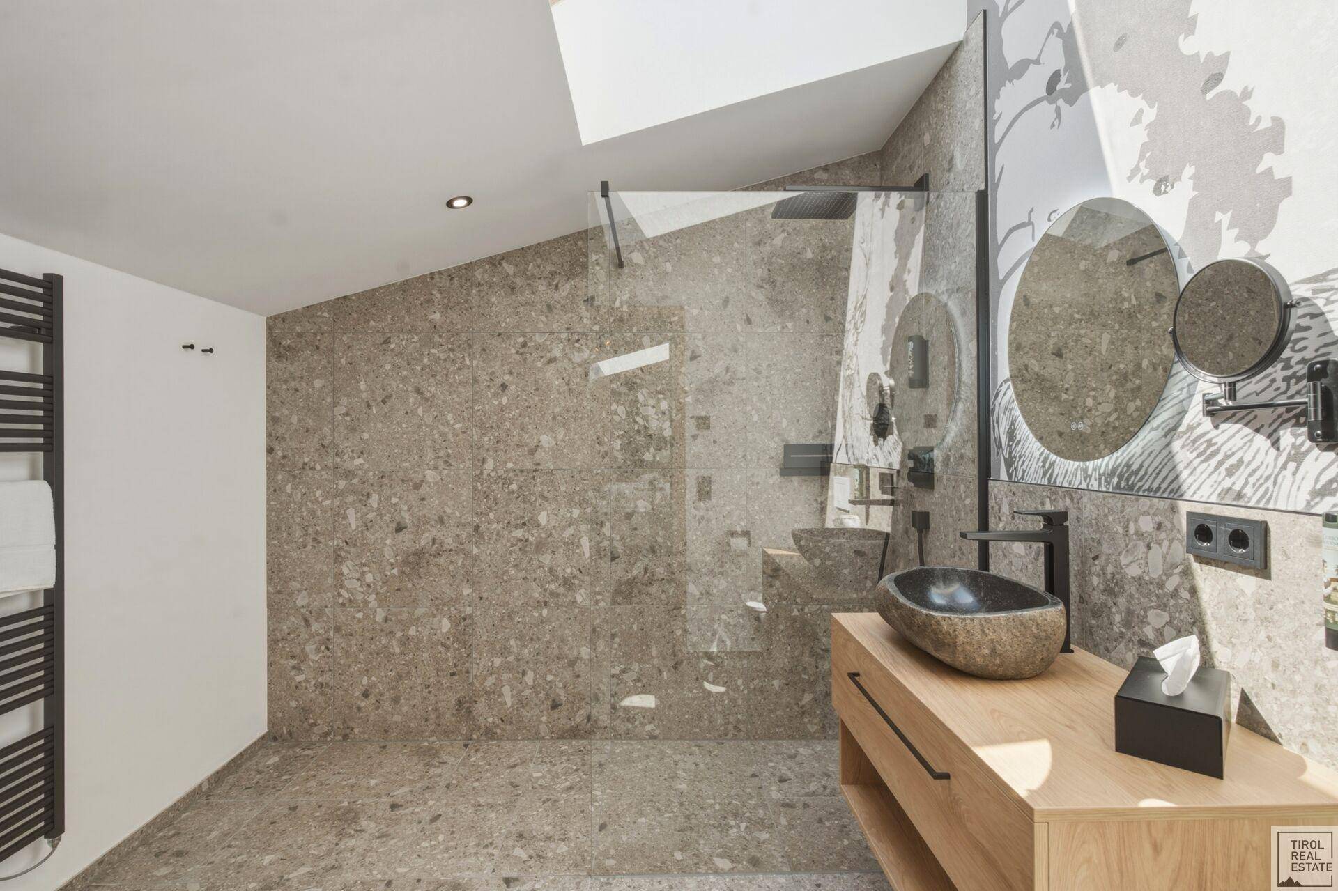 Geräumiges Badezimmer mit Steinfliesen, großer begehbarer Dusche und beheiztem Handtuchhalter.