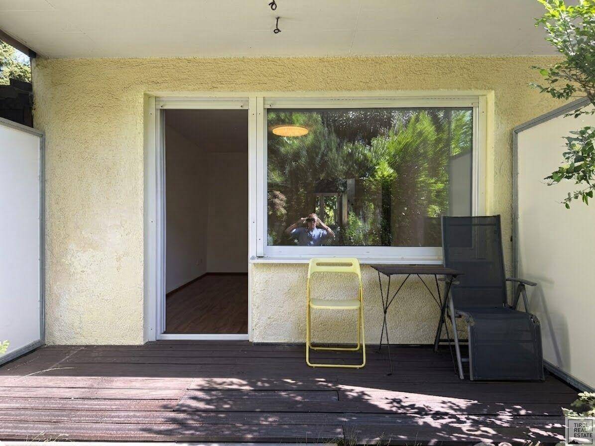 Sonnige Terrasse mit Holzdielen und Gartenmöbeln, bietet direkten Zugang zum Innenbereich.