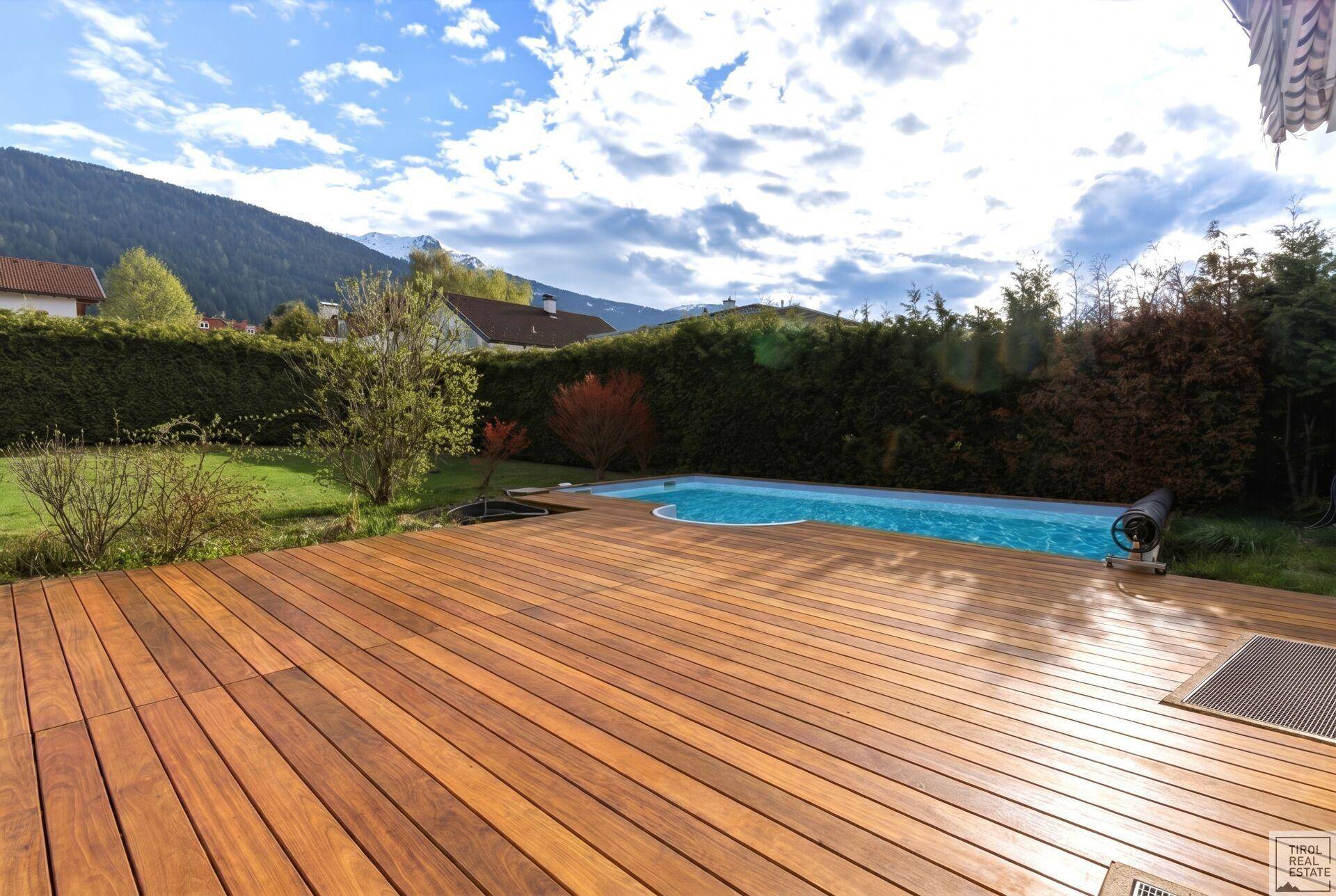 Große Holzterrasse am Pool mit Blick auf die umliegende Berglandschaft und grüne Natur.