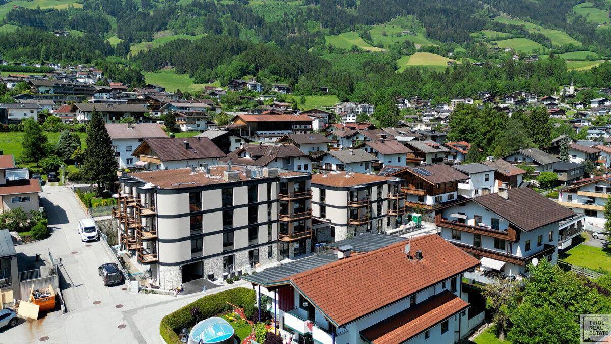 Luftaufnahme einer Wohnsiedlung in einer grünen Talumgebung mit Bergen im Hintergrund.