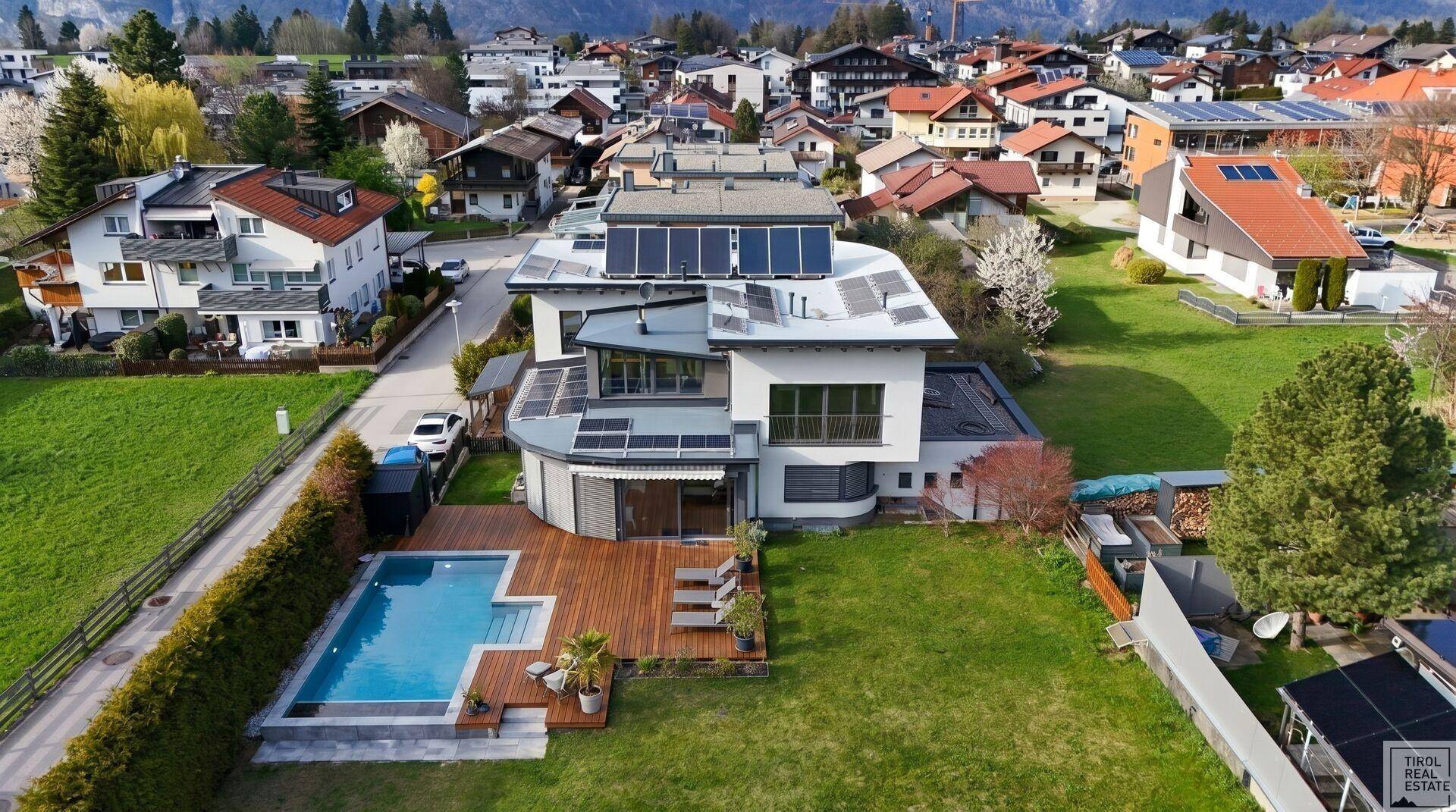Luftaufnahme des modernen Hauses mit Pool, Holzterrasse und großem Garten in alpiner Umgebung.