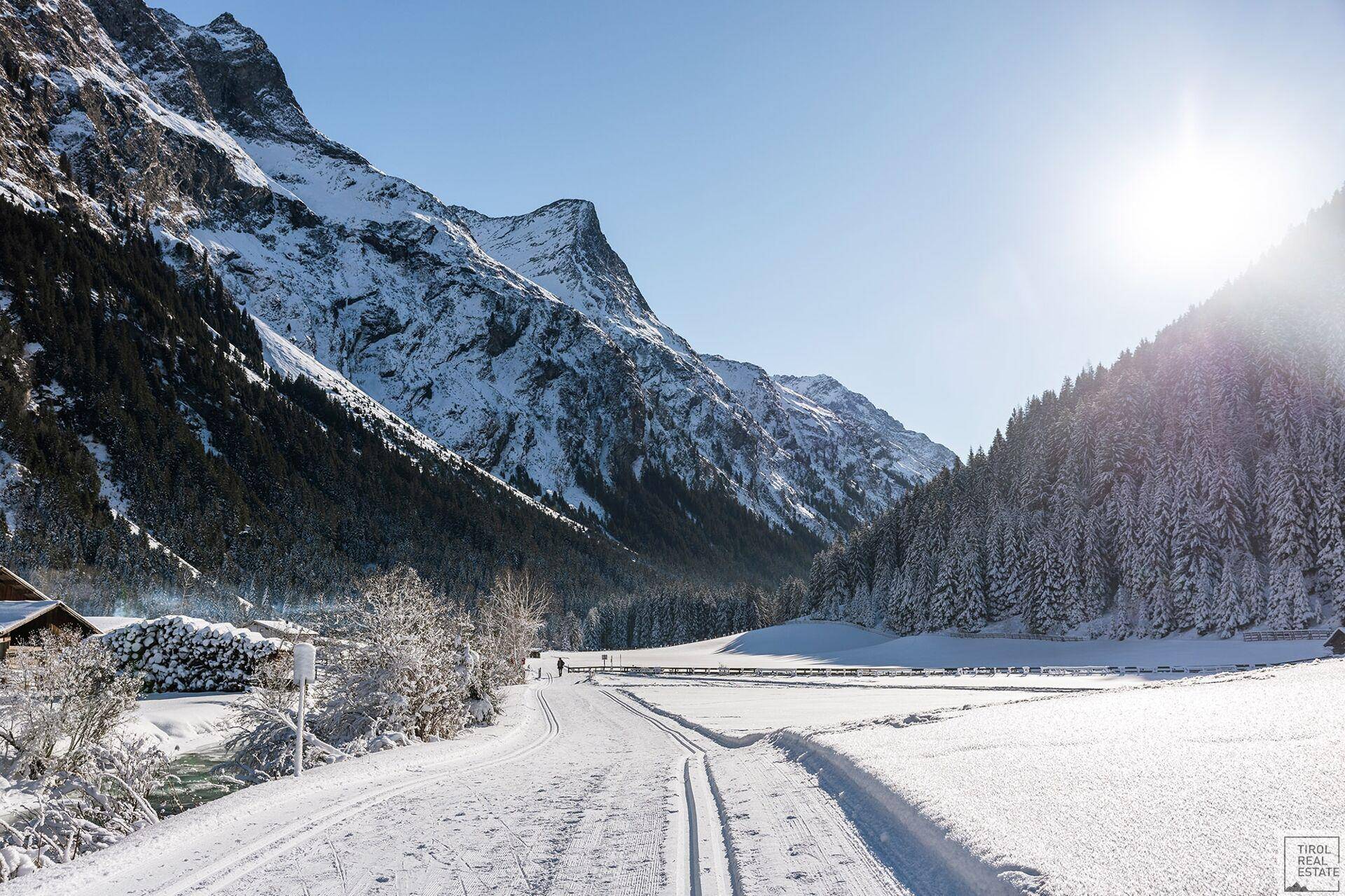 Verschneites Tal mit Langlaufloipe und majestätischen, sonnenbeschienenen Bergen.