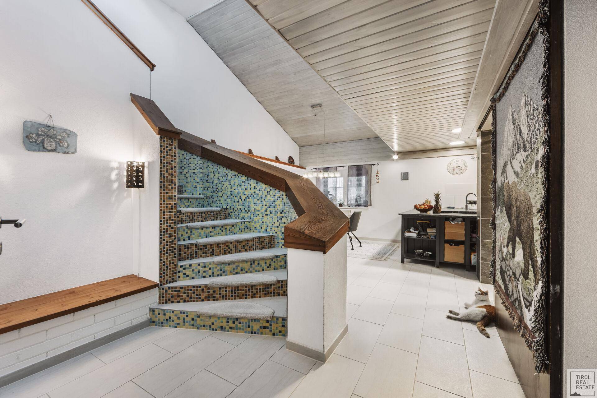 Heller Eingangsbereich mit gefliester Treppe und Holzbalkendecke.