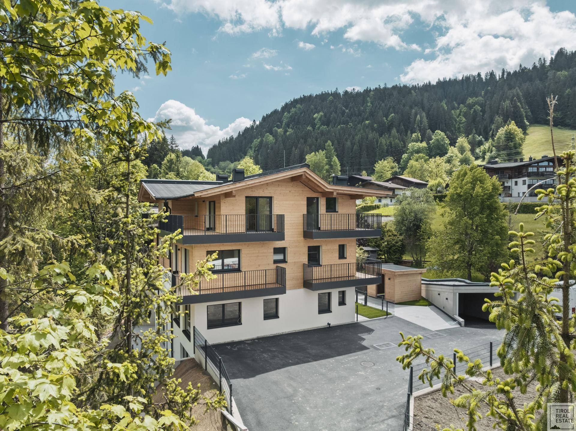 Neubau in alpiner Umgebung mit Holzfassade, Balkonen und Blick auf bewaldete Hügel.