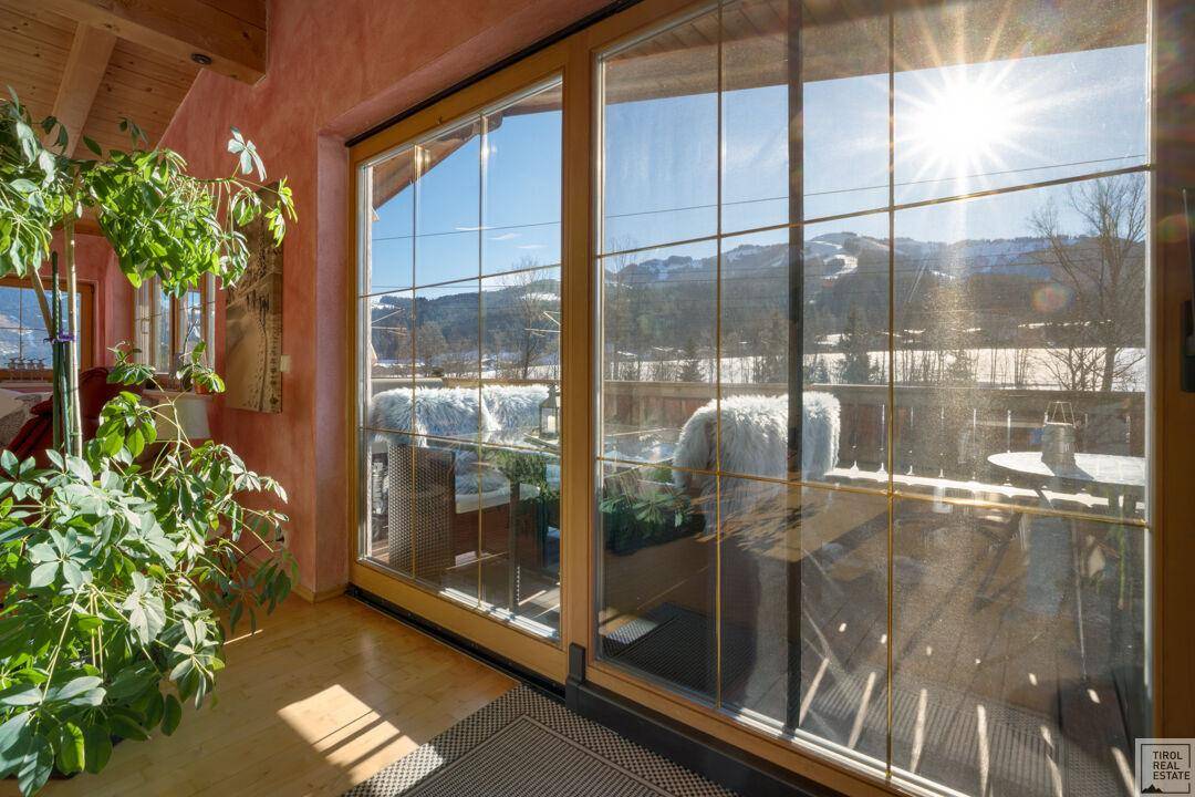 Heller Innenraum mit großen Fenstern und sonnigem Blick auf die verschneite Berglandschaft.