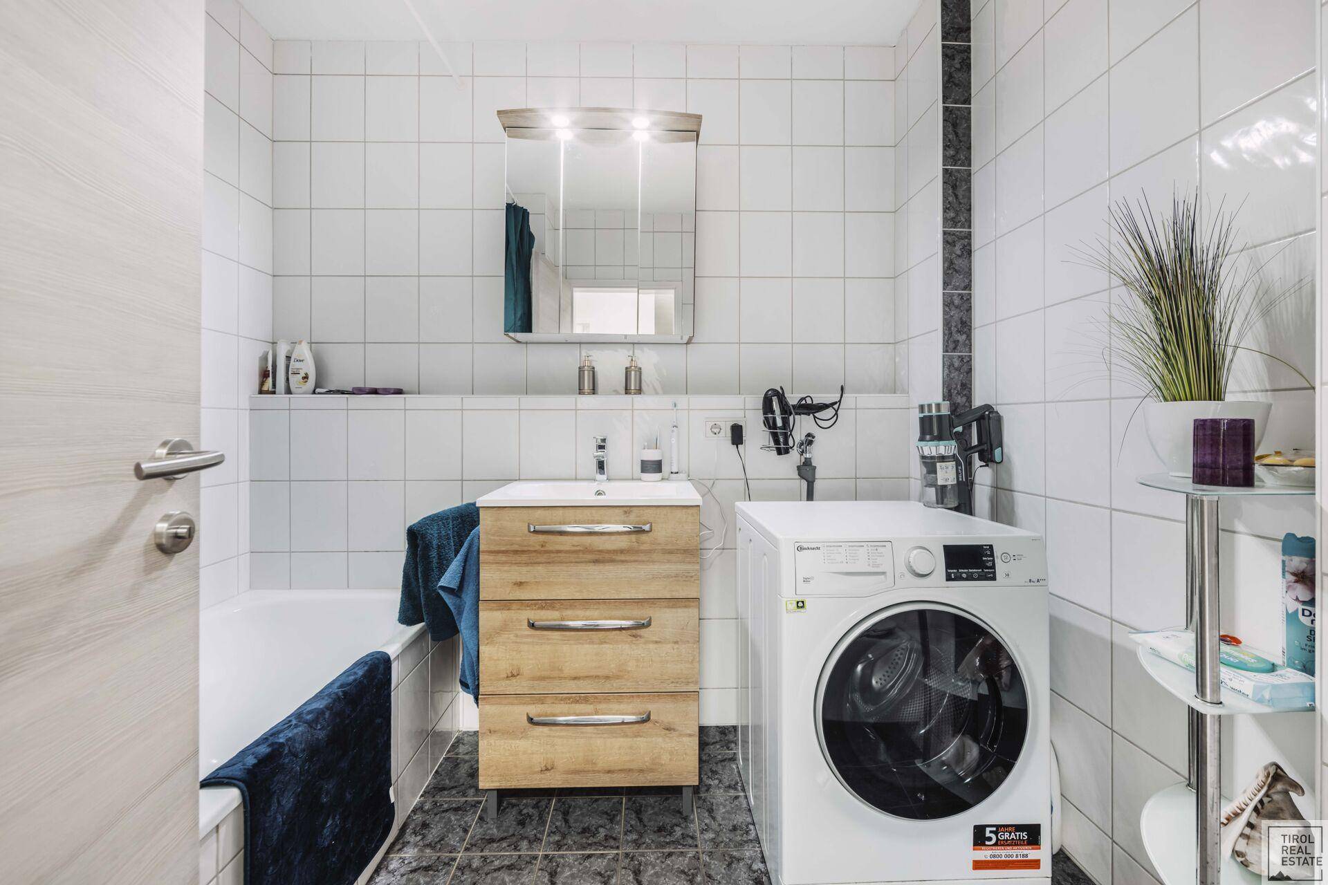 Badezimmer mit Badewanne, Waschbecken und Waschmaschine, komplett gefliest.