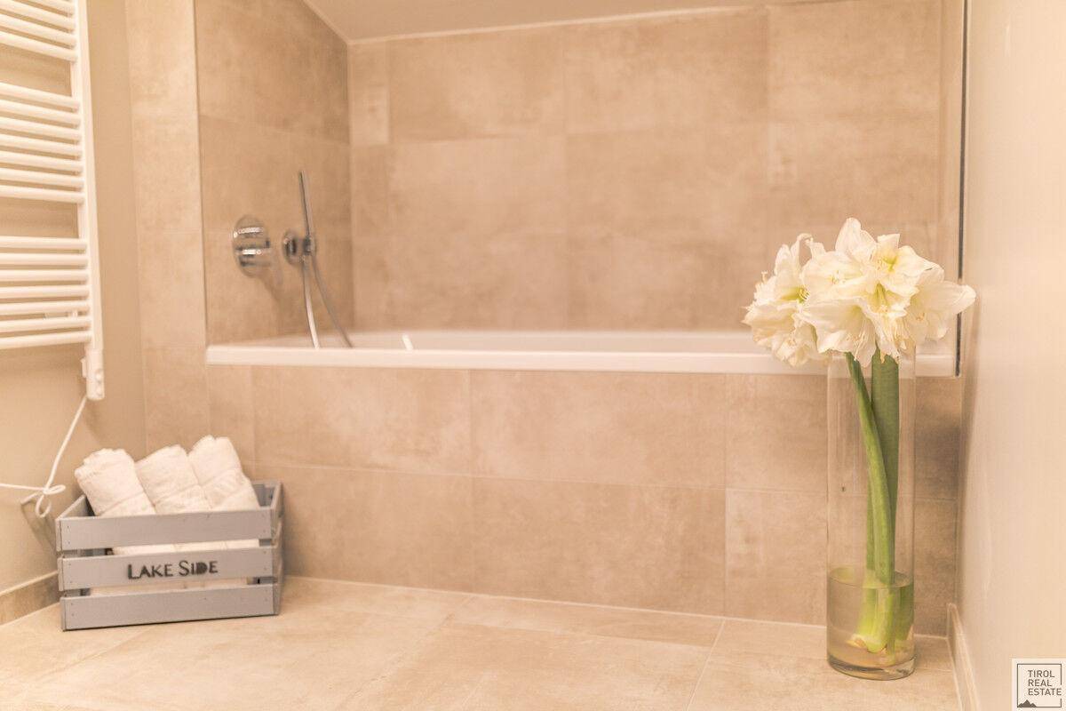 Detailansicht der Badewanne in einem hellen Badezimmer mit beigefarbenen Fliesen und Handtüchern.