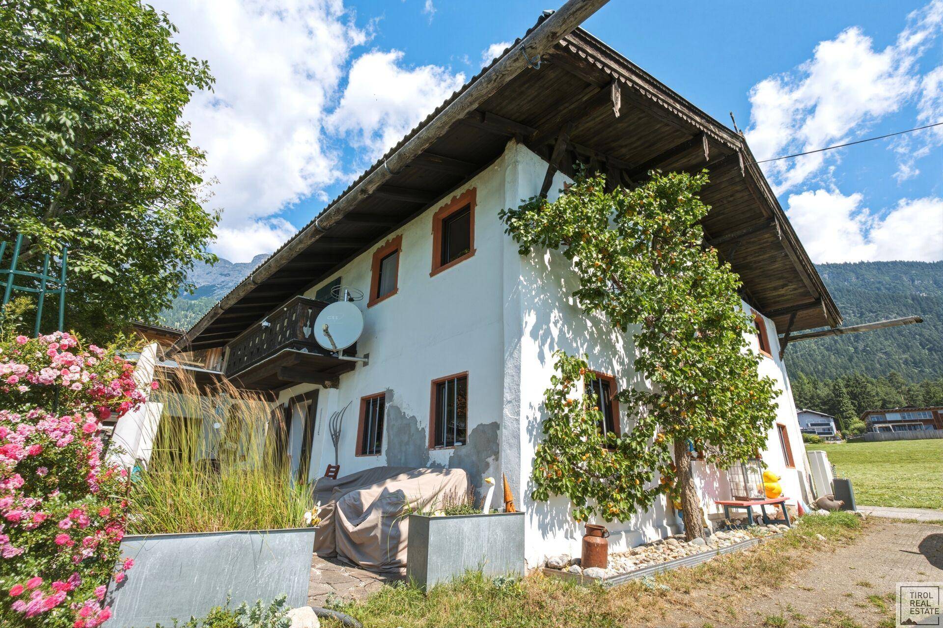 Traditionelles Bauernhaus mit weißer Fassade, Holzbalkon und blühenden Rosen.