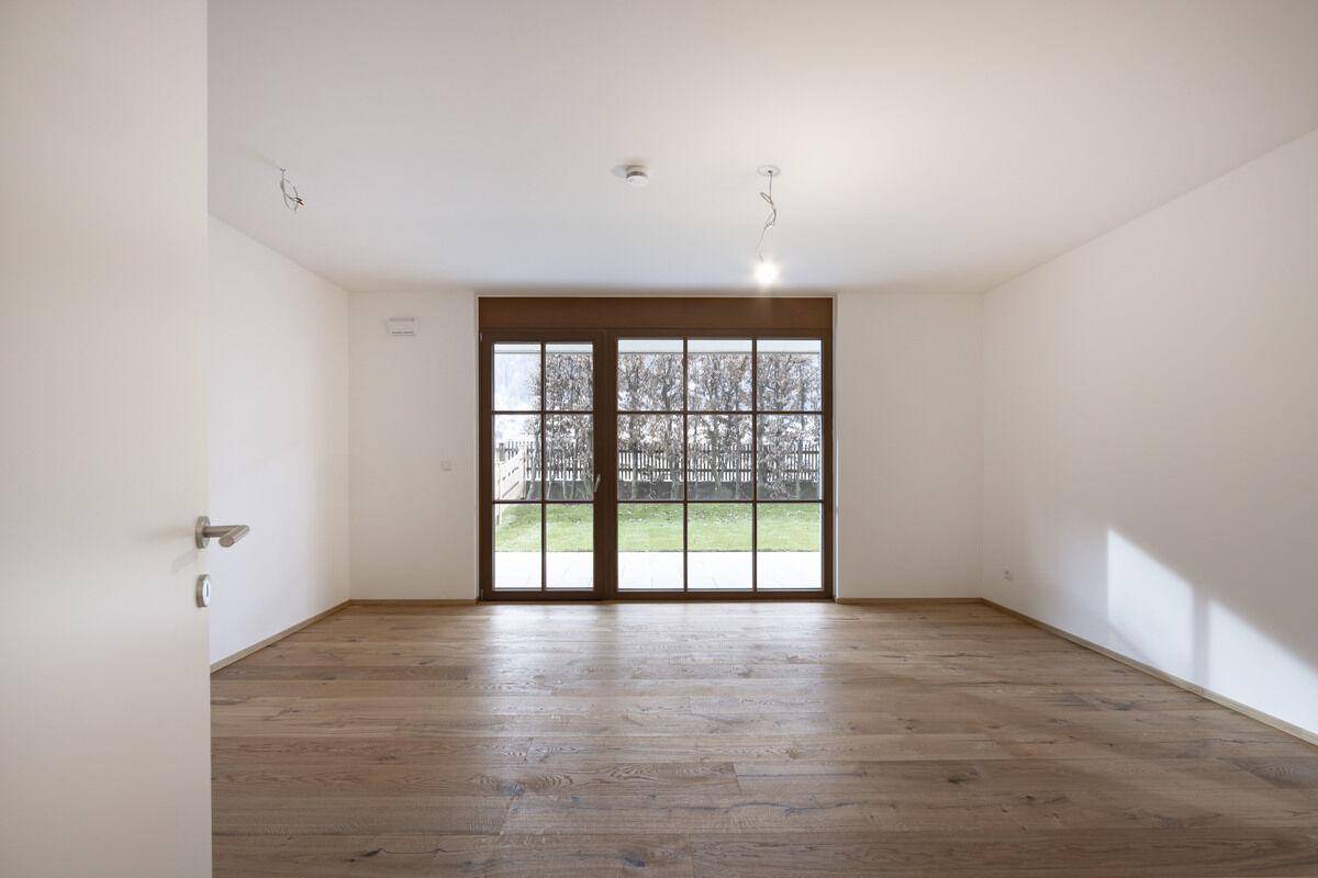 Unmöblierter Raum mit großen Fenstern, die viel Tageslicht hereinlassen und einen Blick ins Grüne bieten.