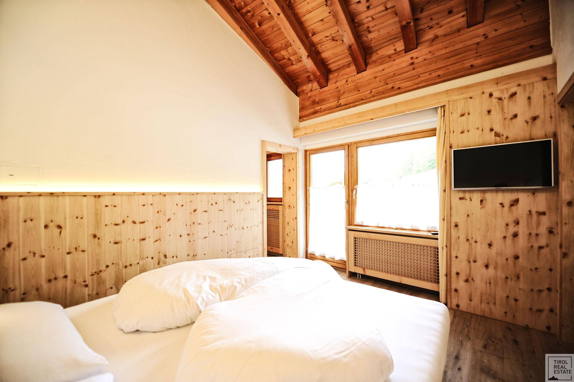 Gemütliches Schlafzimmer mit Holzbalkendecke, Holzvertäfelung und einem großen Fenster, das viel Licht hereinlässt.