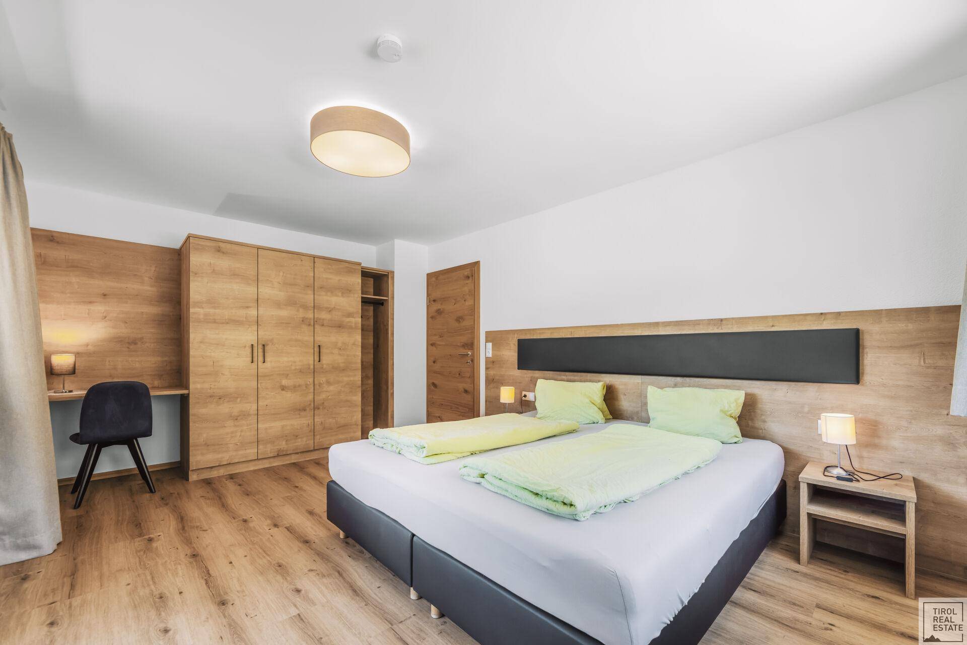 Helles Schlafzimmer mit Doppelbett, Holzschrank und Schreibtisch in modernem Design.