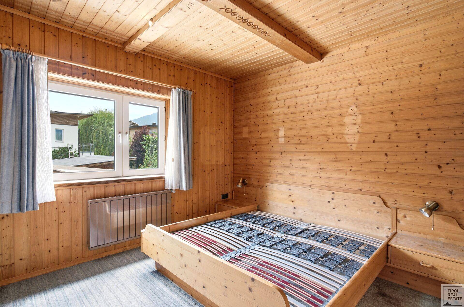 Gemütliches Schlafzimmer mit Holzwänden, Holzbalkendecke und einem großen Fenster.