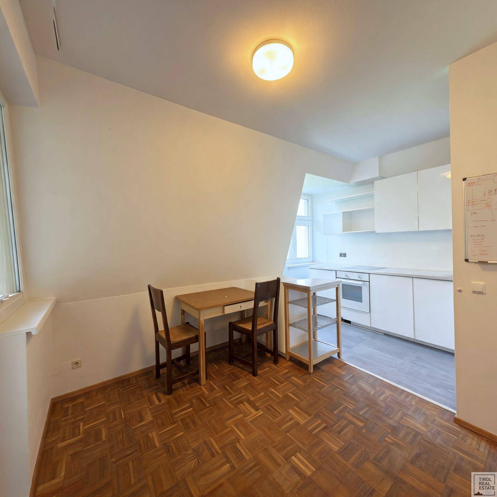 Essbereich mit Holztisch und Stühlen, der nahtlos in eine moderne, weiße Küche übergeht.