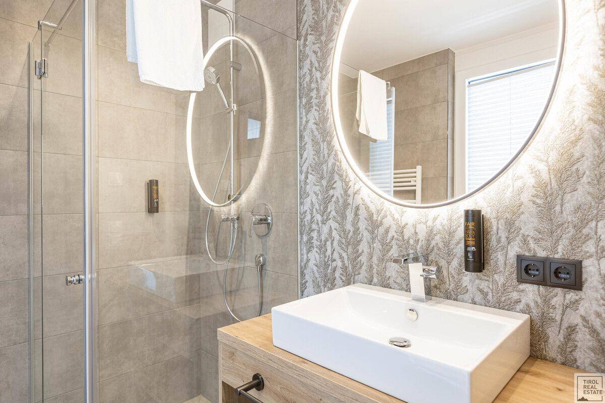 Modernes Badezimmer mit begehbarer Dusche, beleuchtetem Spiegel und Holzwaschtisch.