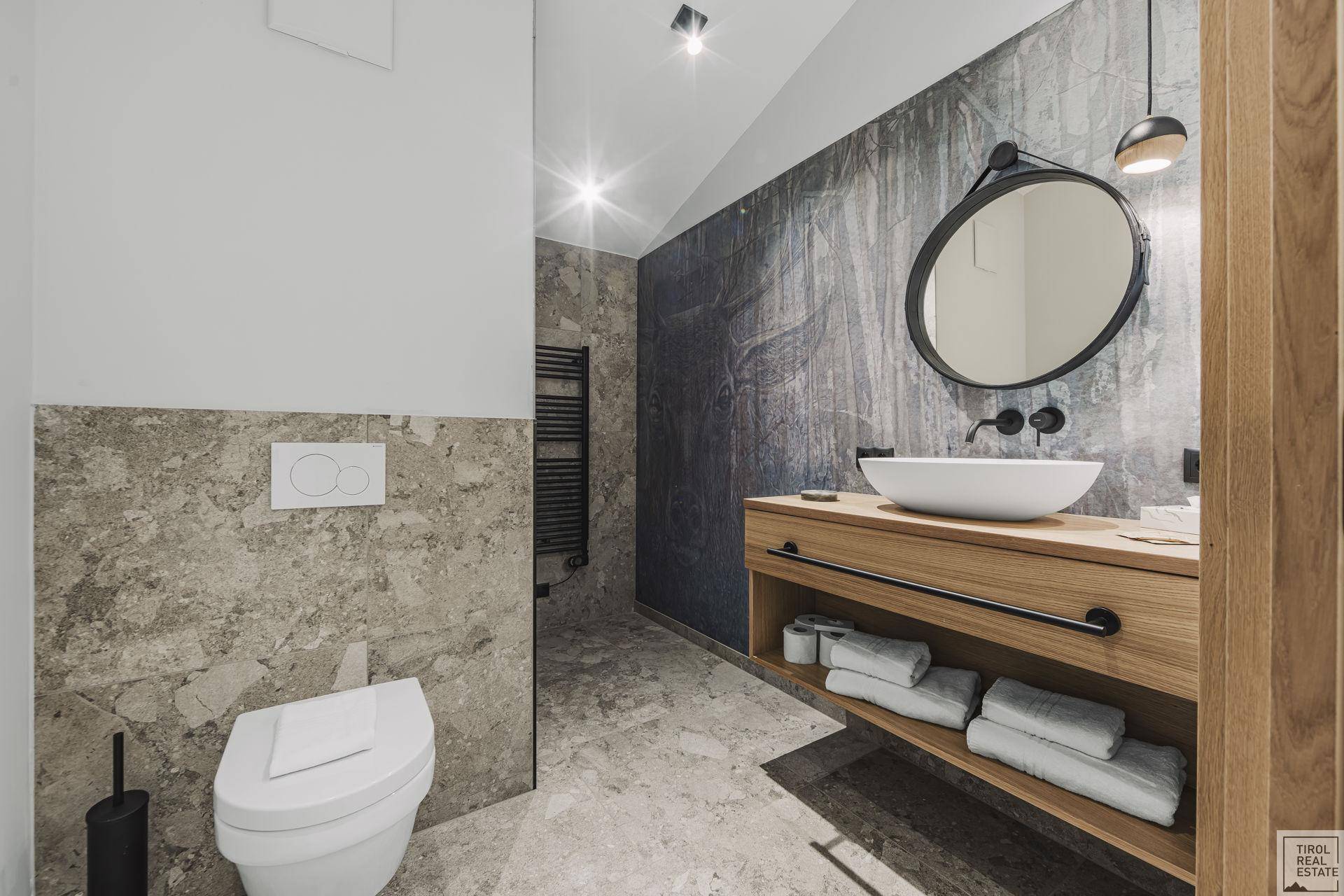 Stilvolles Badezimmer mit Wand-WC, modernem Waschtisch und großformatigen Fliesen sowie einem Handtuchheizkörper.