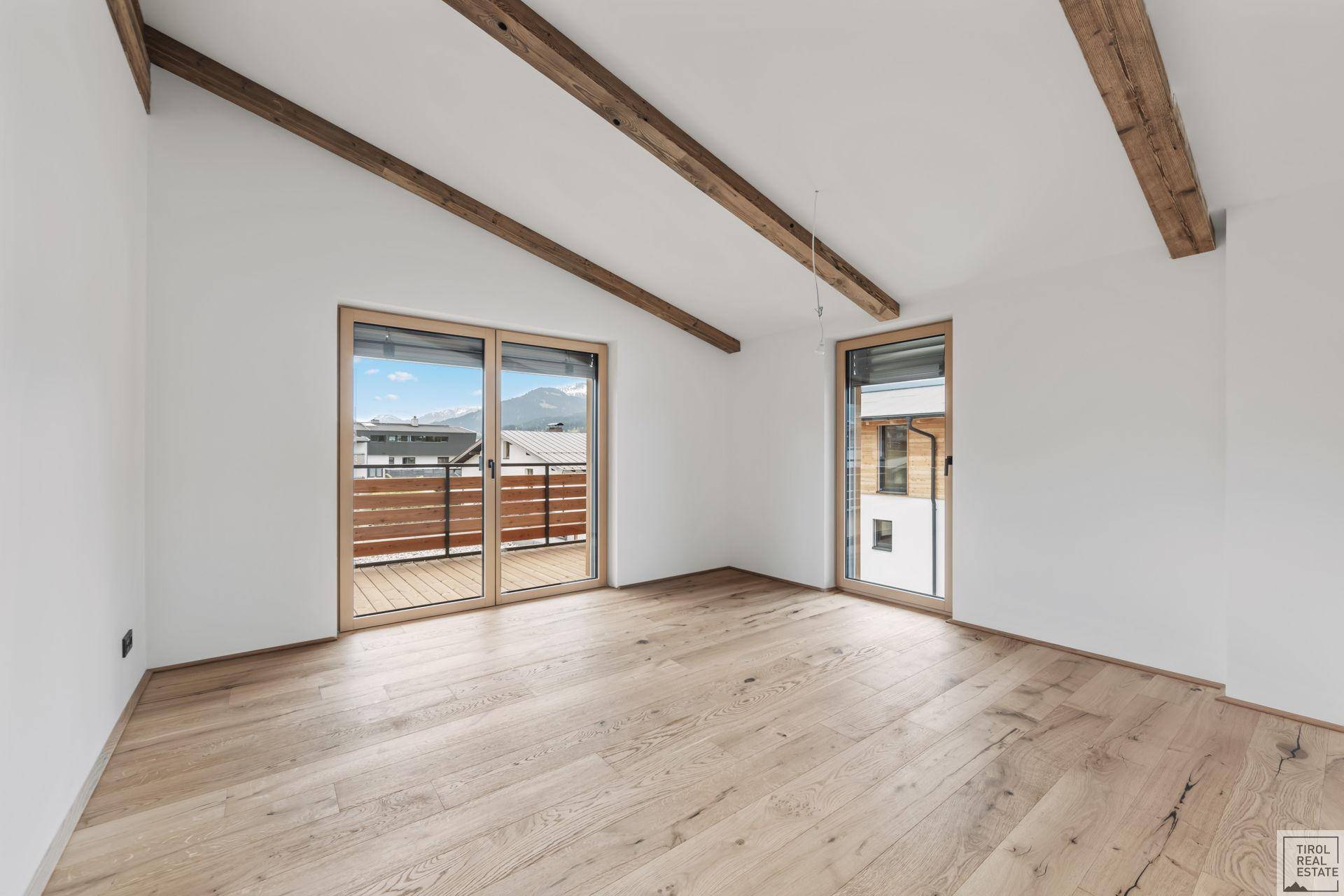 Helles Zimmer mit Holzbalken, Parkettboden und Zugang zu einem Balkon oder einer Terrasse.