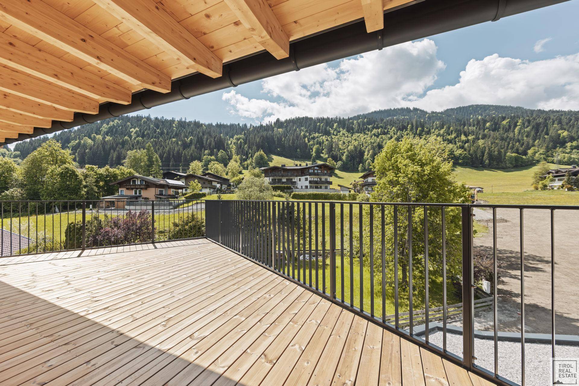 Sonniger Holzbalkon mit weitem Blick über grüne Wiesen und die umliegende Landschaft.