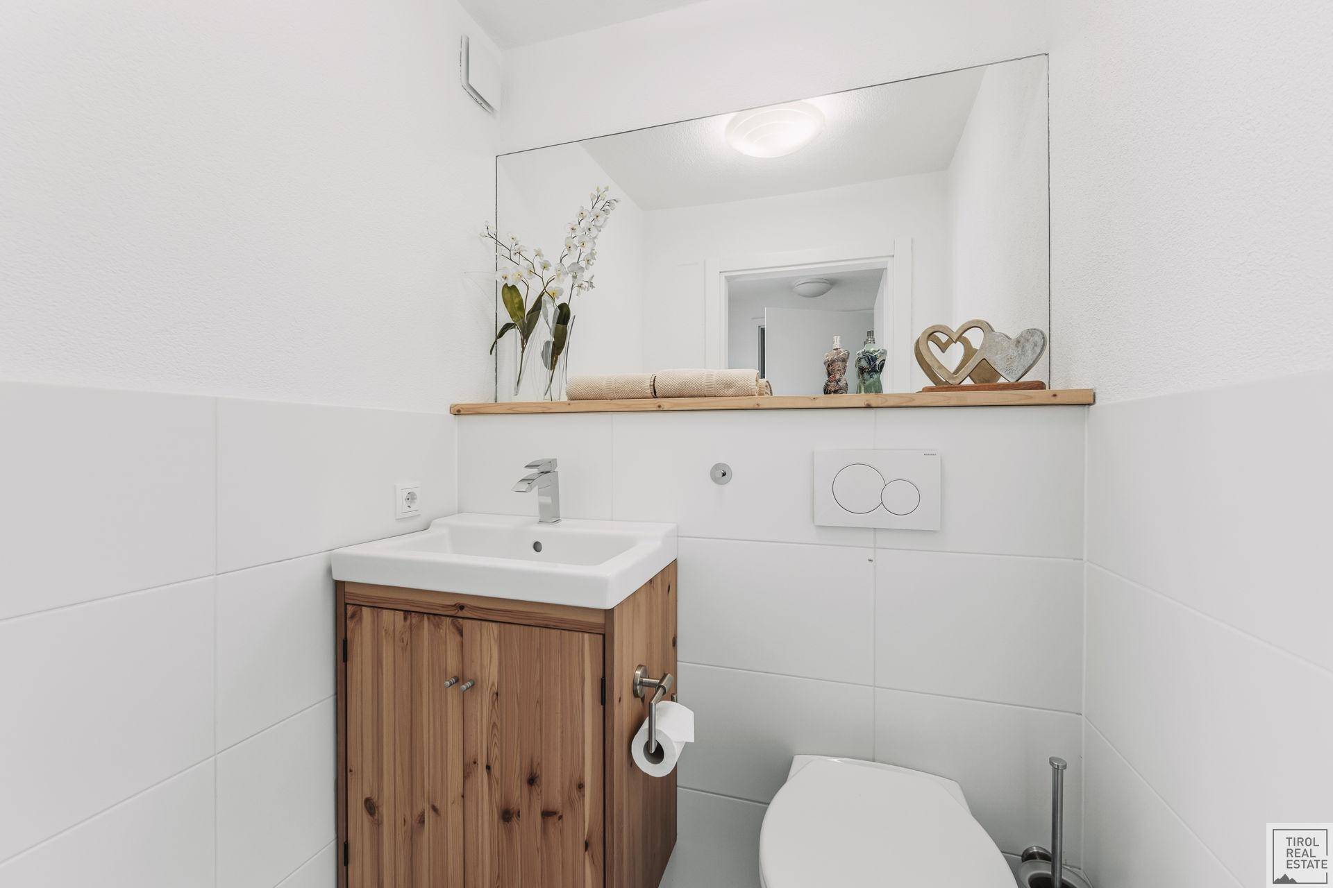 Kleines Gäste-WC mit Holzwaschtisch, Spiegel und weißen Fliesen.