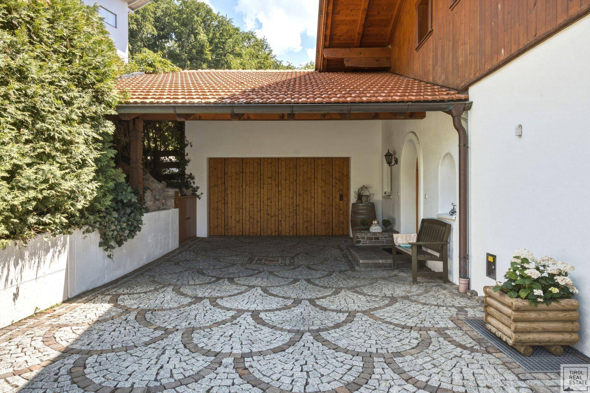 Kunstvoll gepflasterte Auffahrt führt zu einer Holzgarage, umgeben von gepflegten Hecken und Blumen.