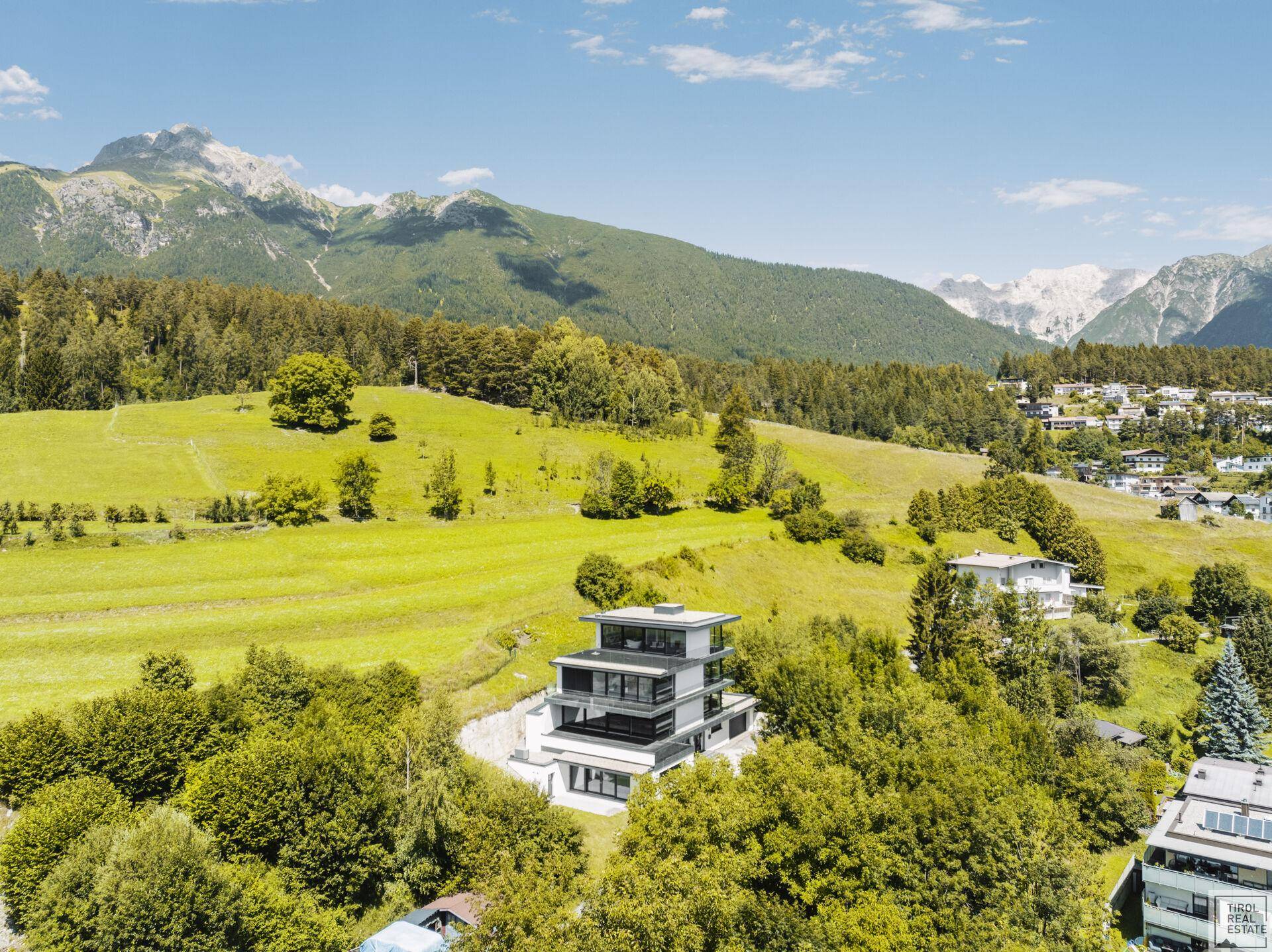 Luftaufnahme der modernen Villa in einer idyllischen Berglandschaft mit umliegenden Häusern.