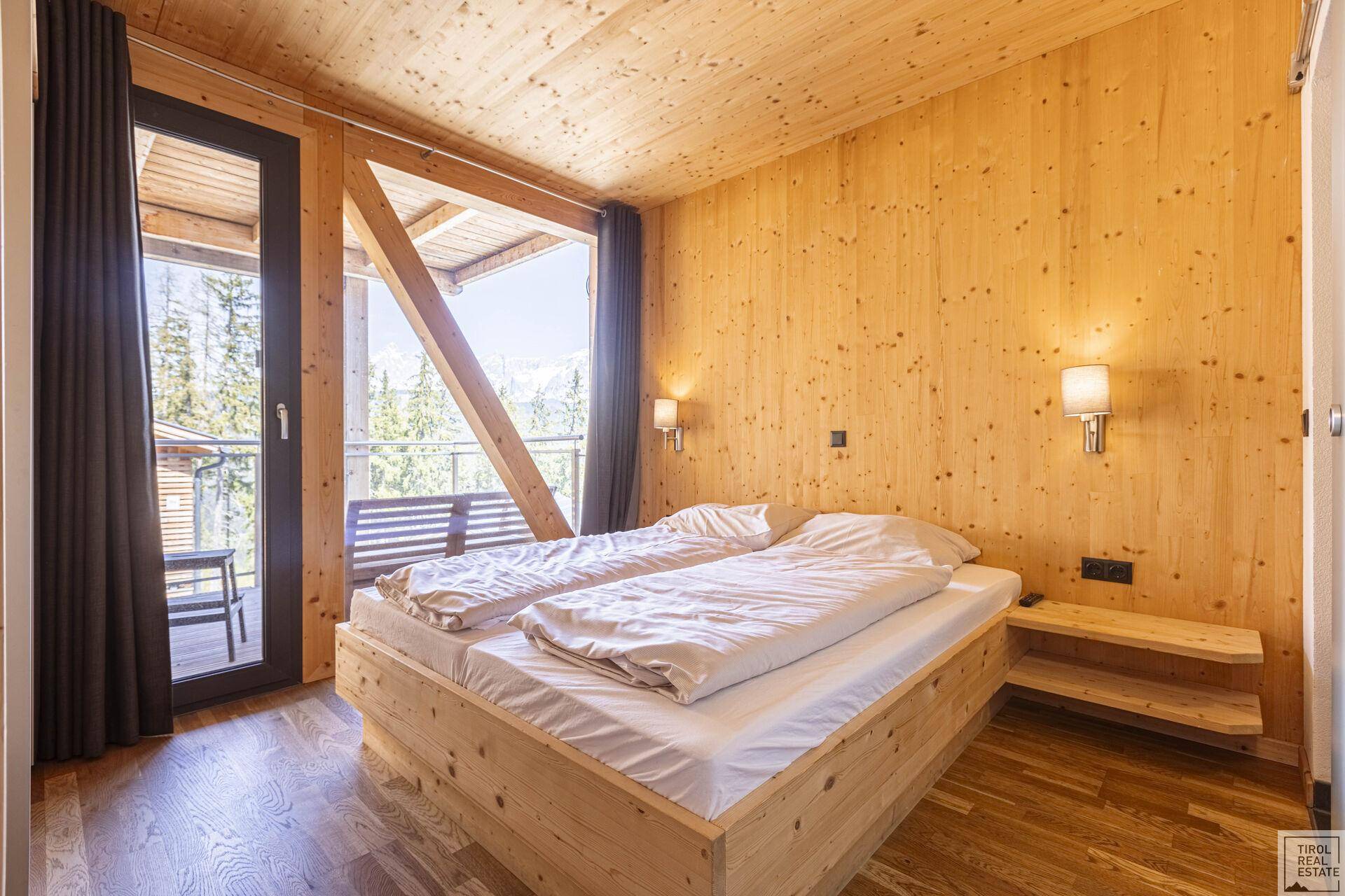 Schlafzimmer im alpinen Stil mit Holzwänden, Doppelbett und Balkonzugang mit Bergblick.