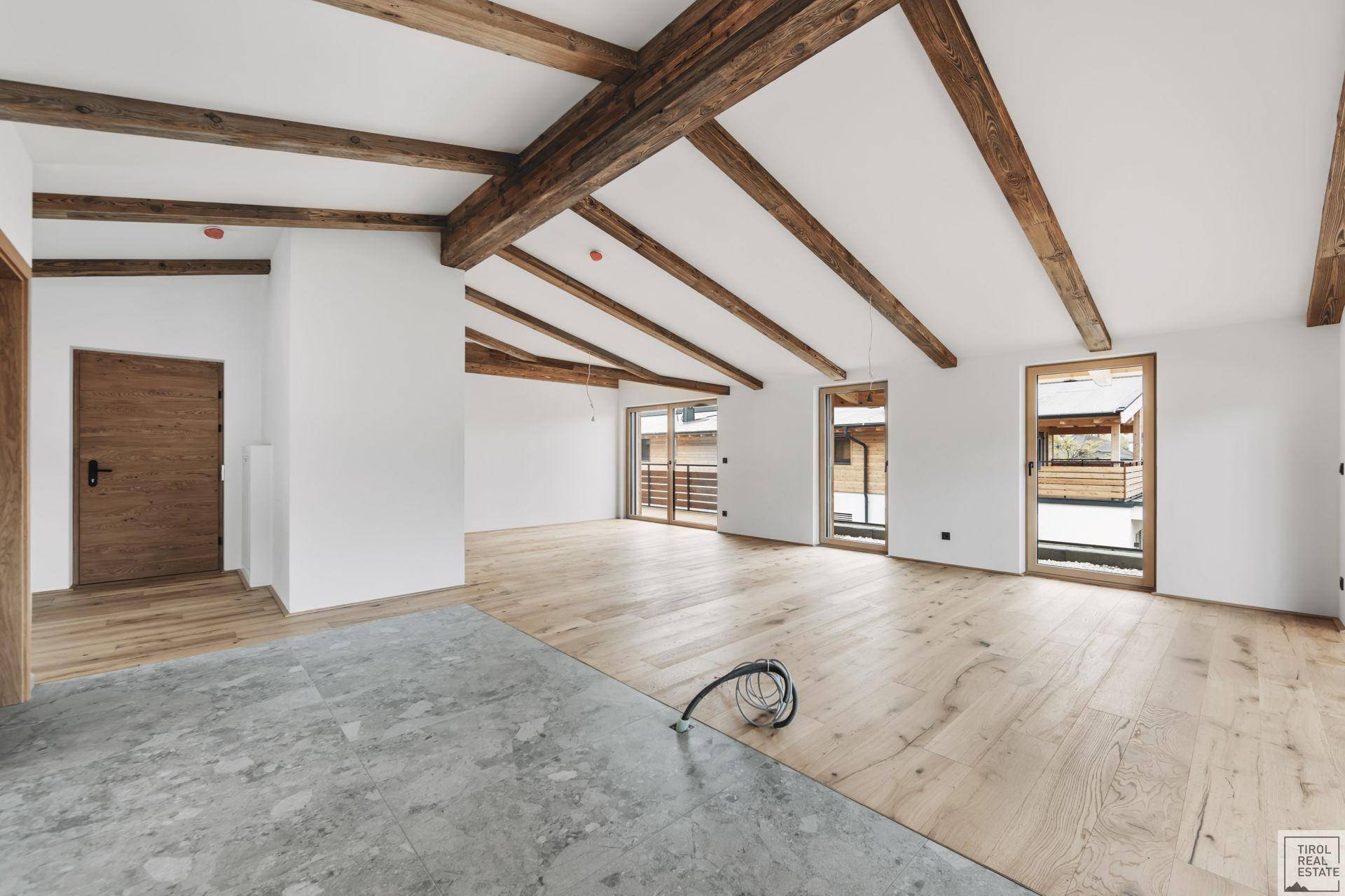 Geräumiger, unmöblierter Innenraum mit sichtbaren Holzbalken und gemischtem Bodenbelag.