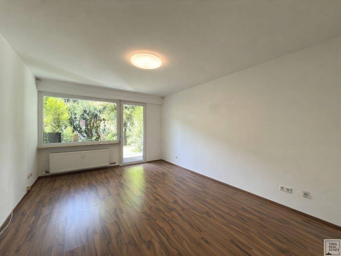 Geräumiges, helles Zimmer mit Holzboden und großem Fenster zum Gartenbereich.