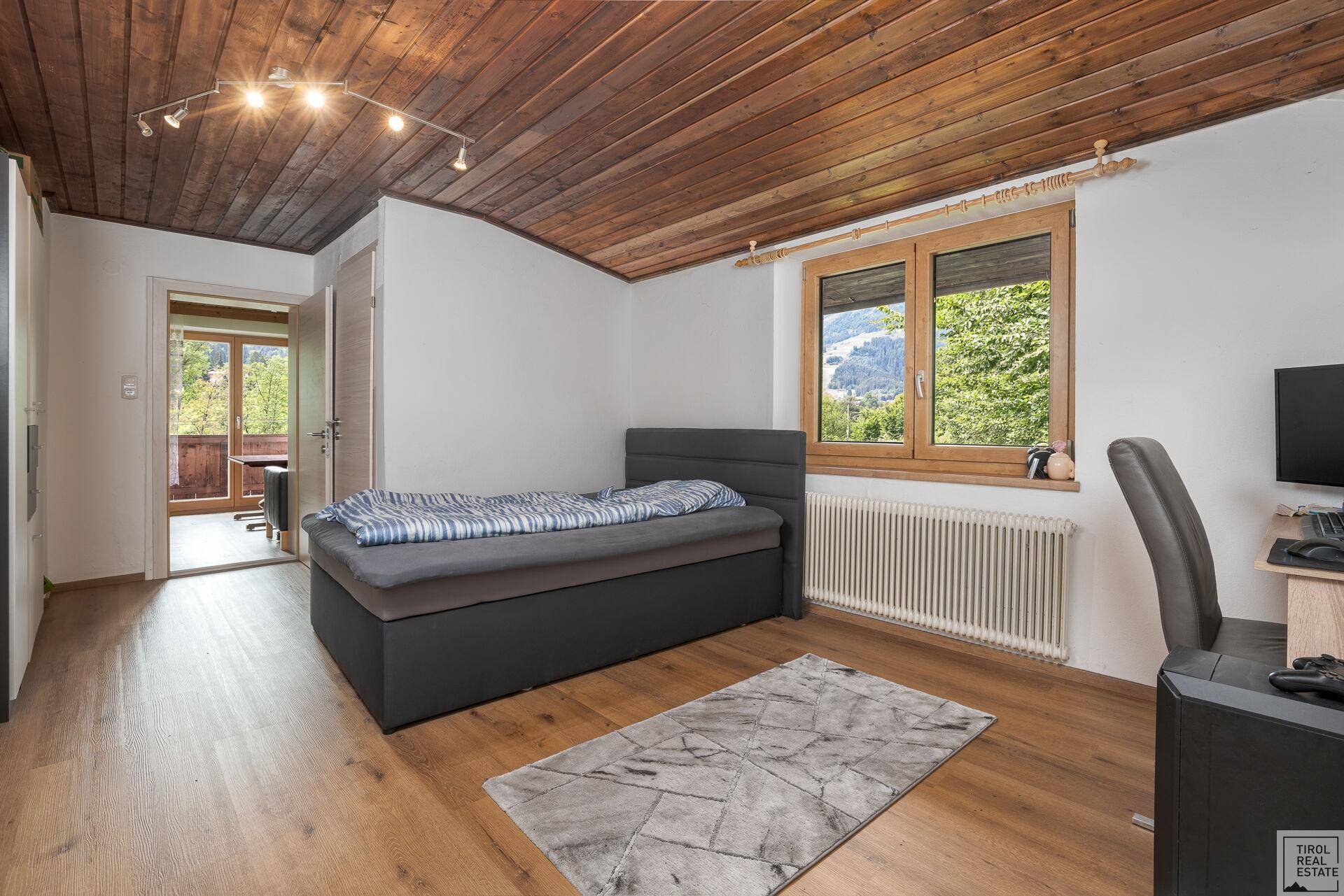 Schlafzimmer mit Einzelbett, Holzboden und Fenster mit Blick auf die grüne Umgebung.