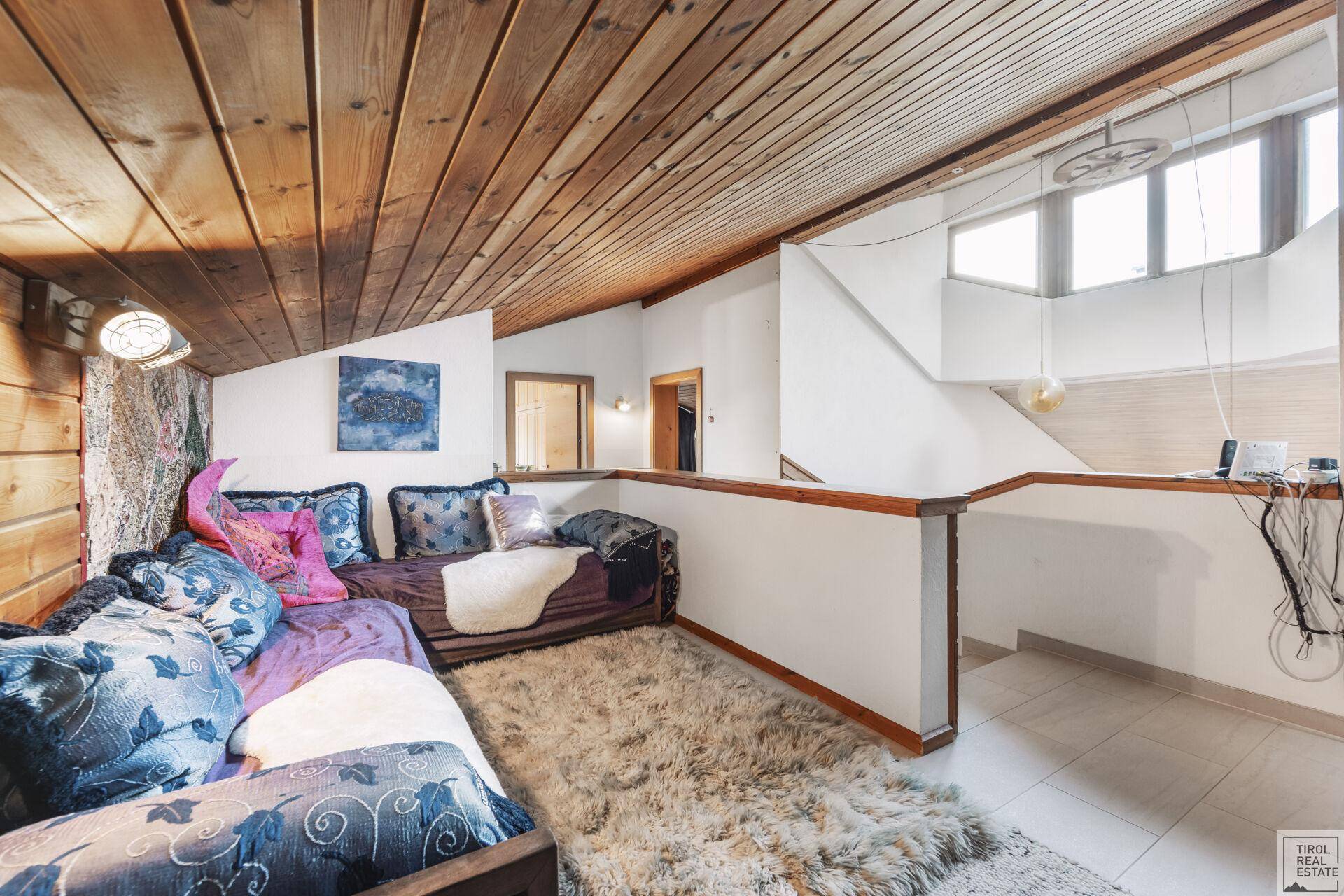 Offener Dachbodenbereich mit Holztäfelung, Teppich und Blick auf die untere Etage.