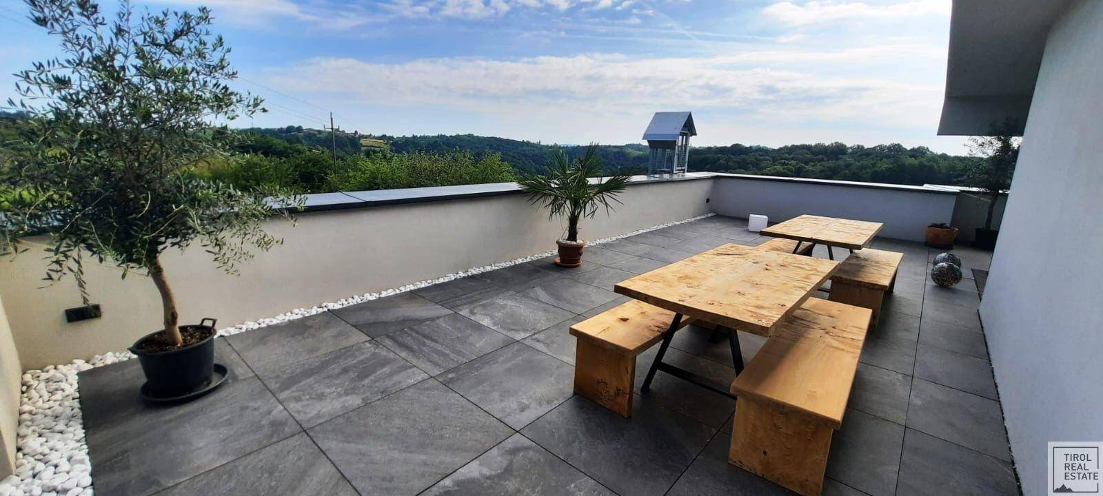 Weitläufige Dachterrasse mit Holztischen, Bänken und Panoramablick auf die Landschaft.