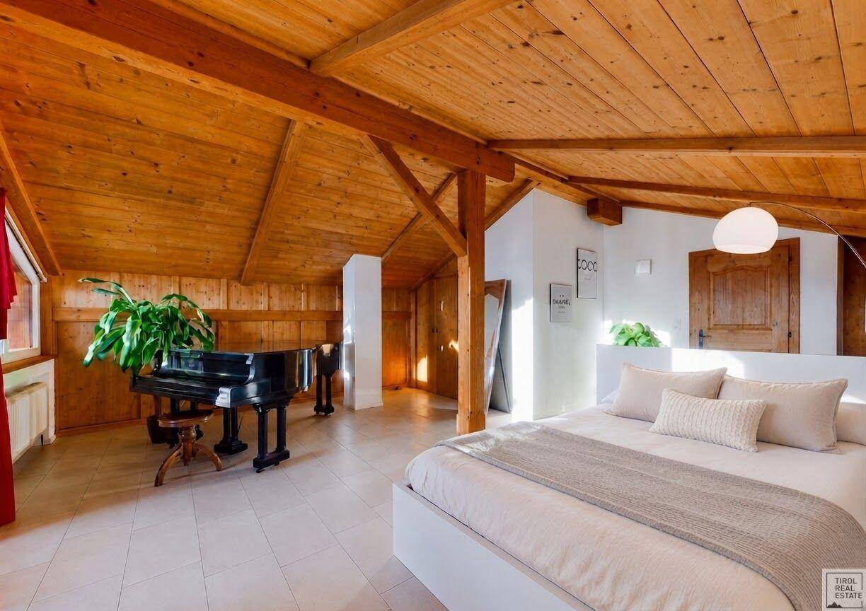 Geräumiges Schlafzimmer im Dachgeschoss mit Holzbalken, Holzdecke und einem Flügel, hell und einladend.