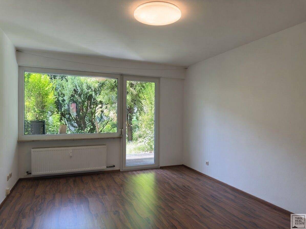Heller Wohnraum mit Holzboden und Zugang zu einem Außenbereich mit viel Grün.