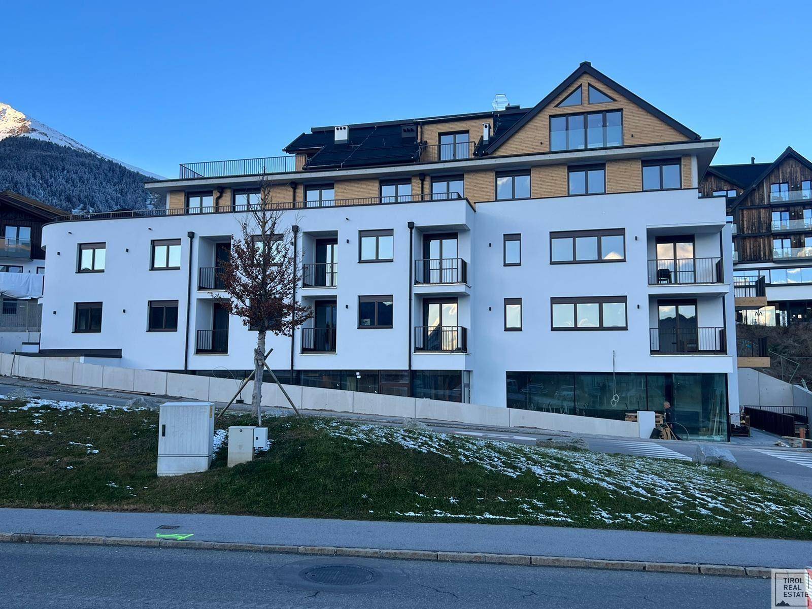 Moderne Wohnanlage mit weißer Fassade, Holzdetails und Balkonen in alpiner Umgebung.