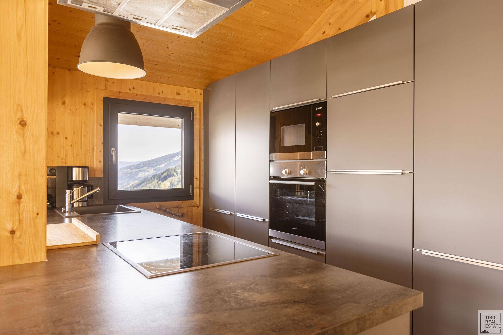 Moderne Einbauküche in Grau mit Backofen, Mikrowelle und Bergblick.
