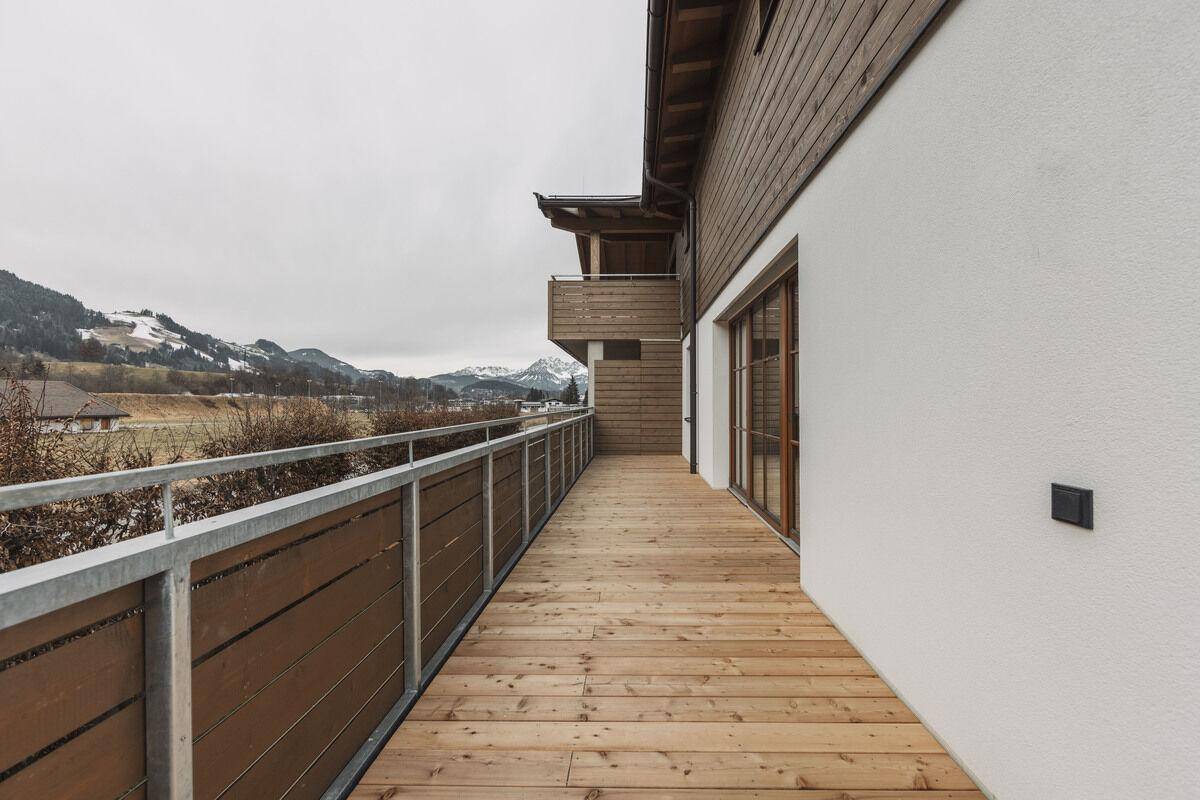 Langer Balkon mit Holzboden und moderner Fassade, bietet einen weiten Blick auf die Umgebung.