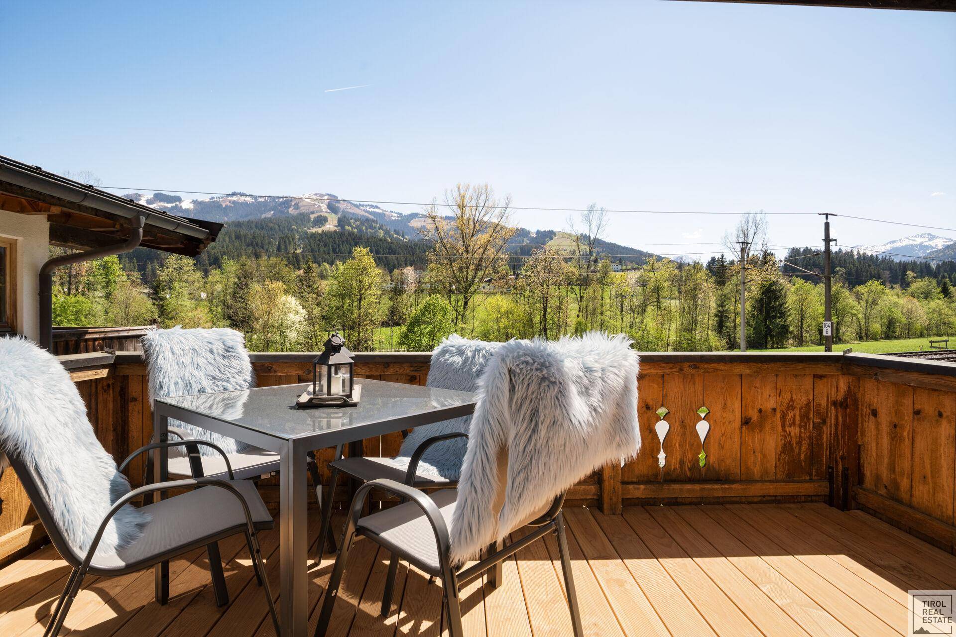 Sonniger Balkon mit Holzboden, Esstisch und weitem Blick auf die grüne Landschaft und Berge.