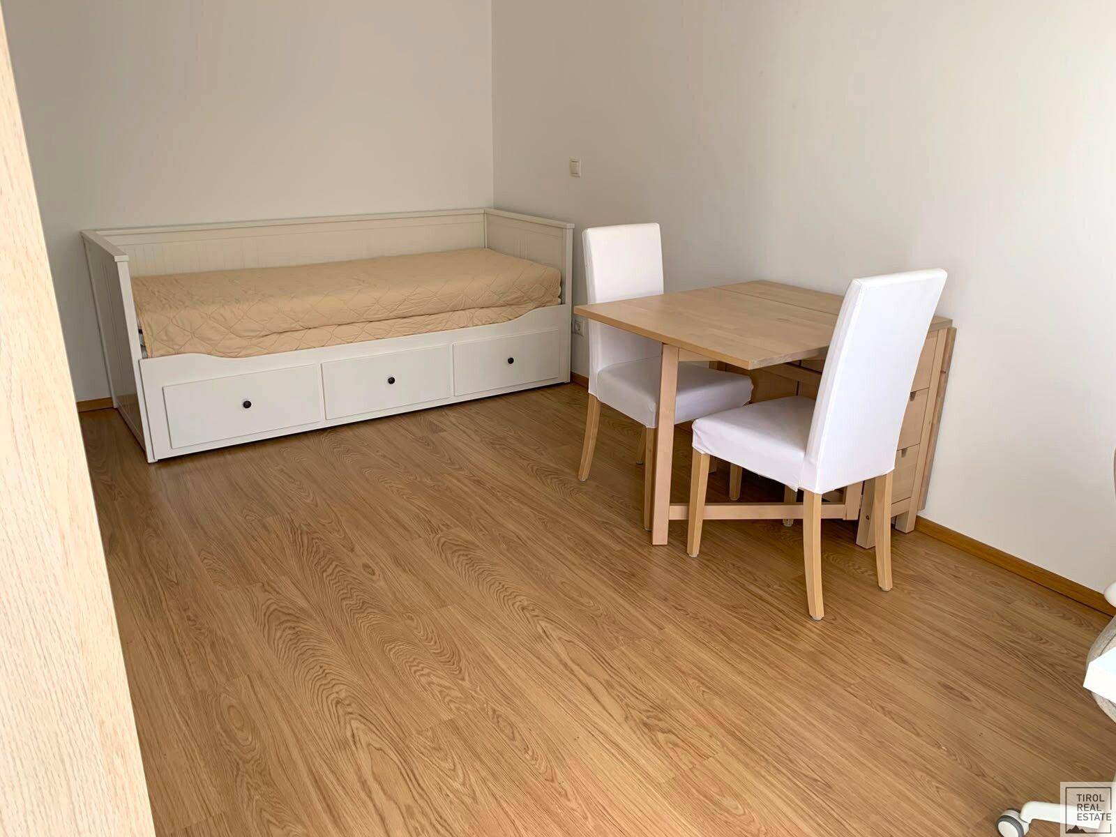 Multifunktionaler Raum mit Tagesbett, Esstisch und hellem Holzboden, geeignet als Schlaf- oder Gästezimmer.
