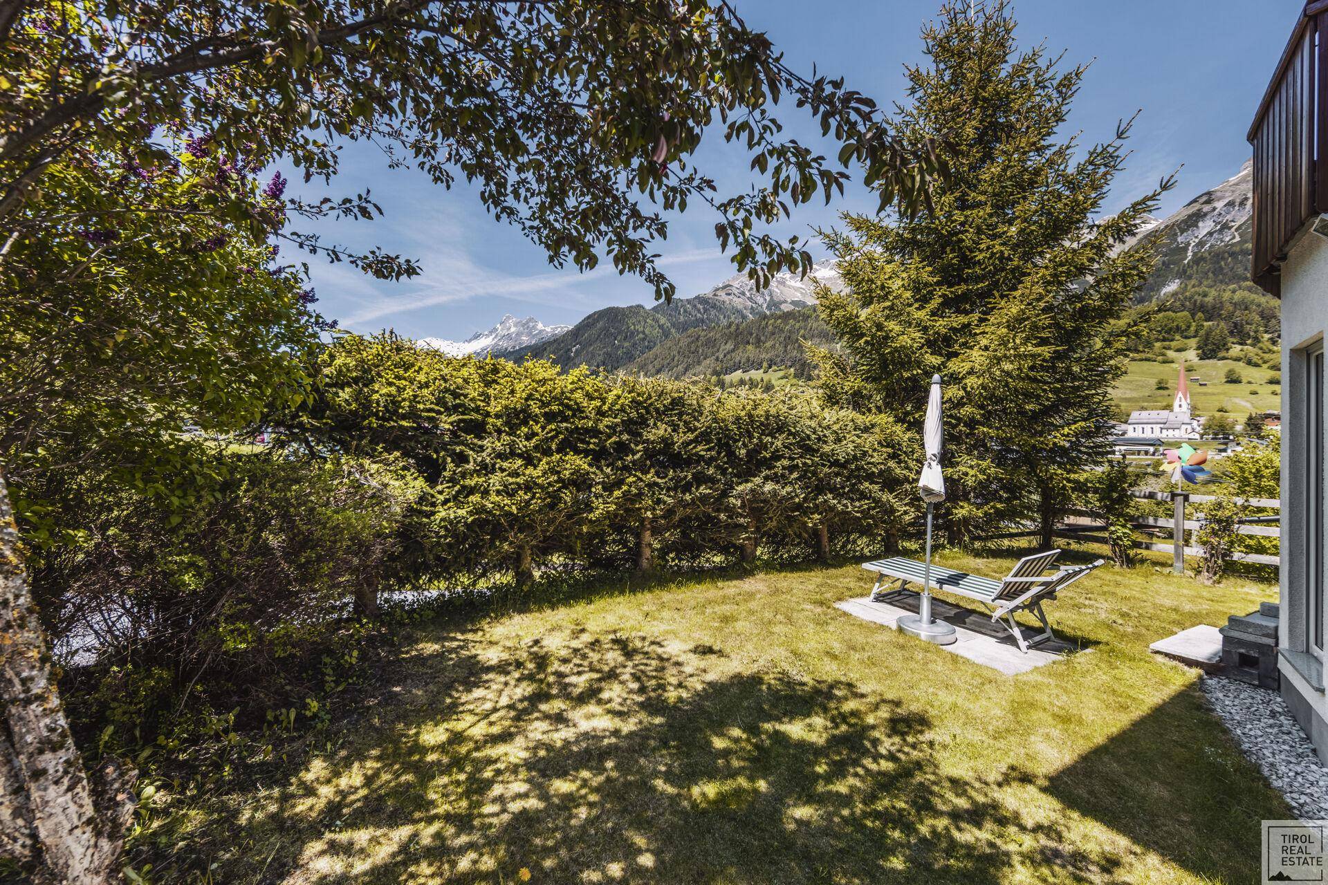 Gepflegter Gartenbereich mit Liegestuhl, Rasenfläche und weitem Blick auf die Berge.