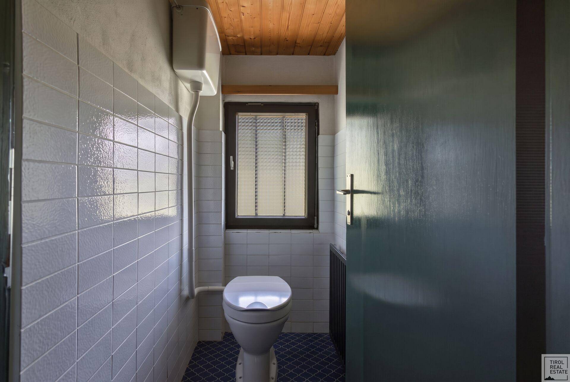 Separate Toilette mit hellblauen Fliesen, Fenster und Holzdecke.