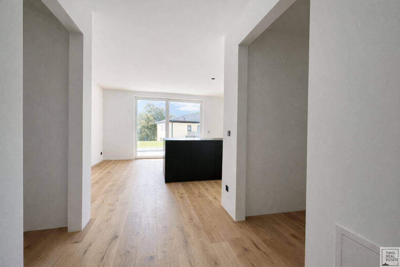 Heller Durchgang zu einem offenen Wohnbereich mit Holzboden und Blick ins Grüne.