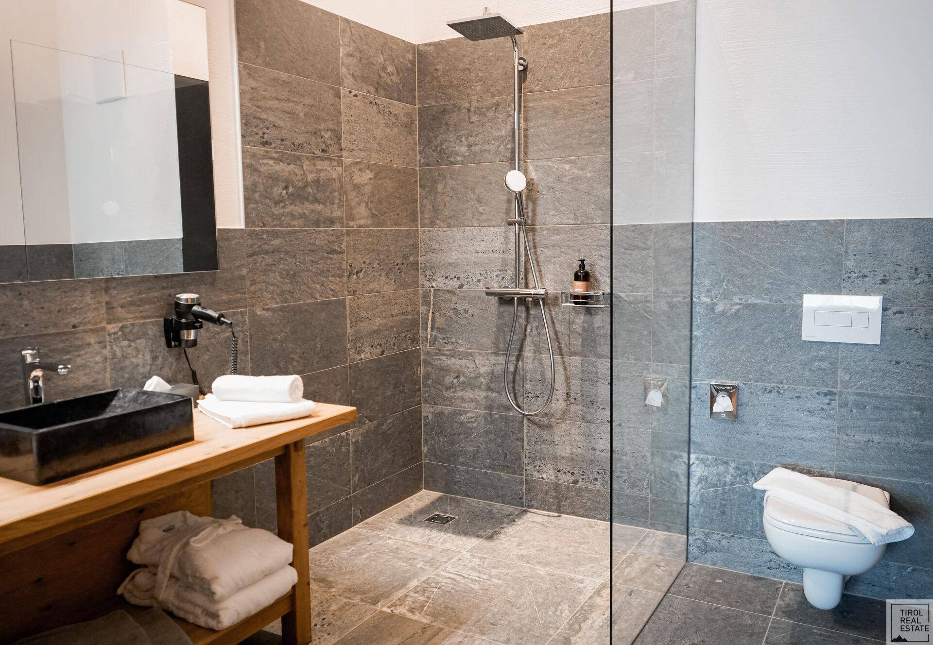 Modernes Badezimmer mit begehbarer Dusche, grauen Fliesen und Holzwaschtisch.