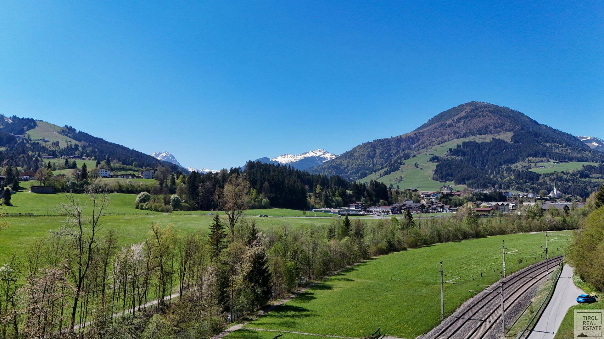 Panoramablick auf die Alpenlandschaft mit grünen Hügeln, Wäldern und einem Flusslauf.